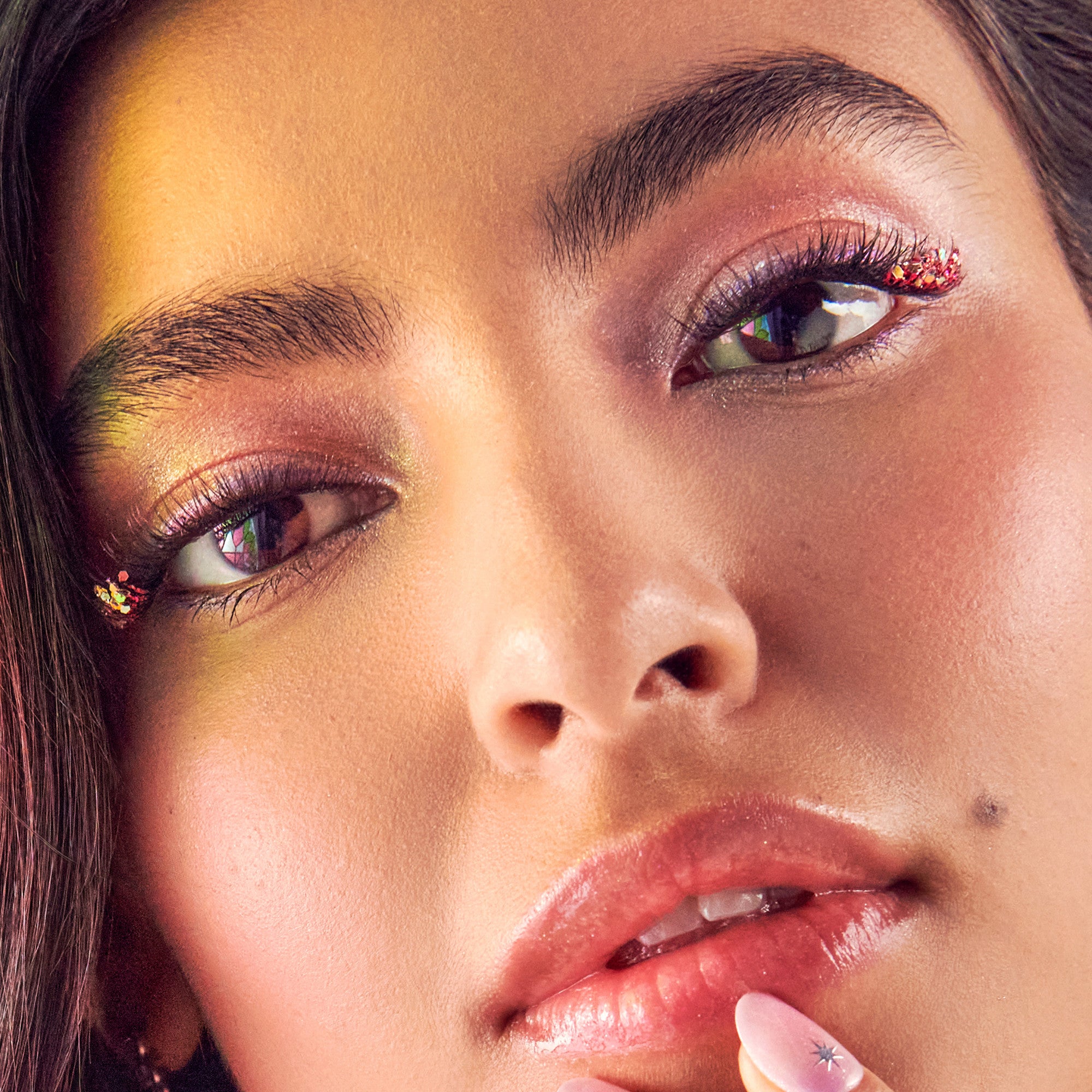 Woman with colorful eyeshadow in gold and burgundy, glittery eye makeup, and red glossy lips.