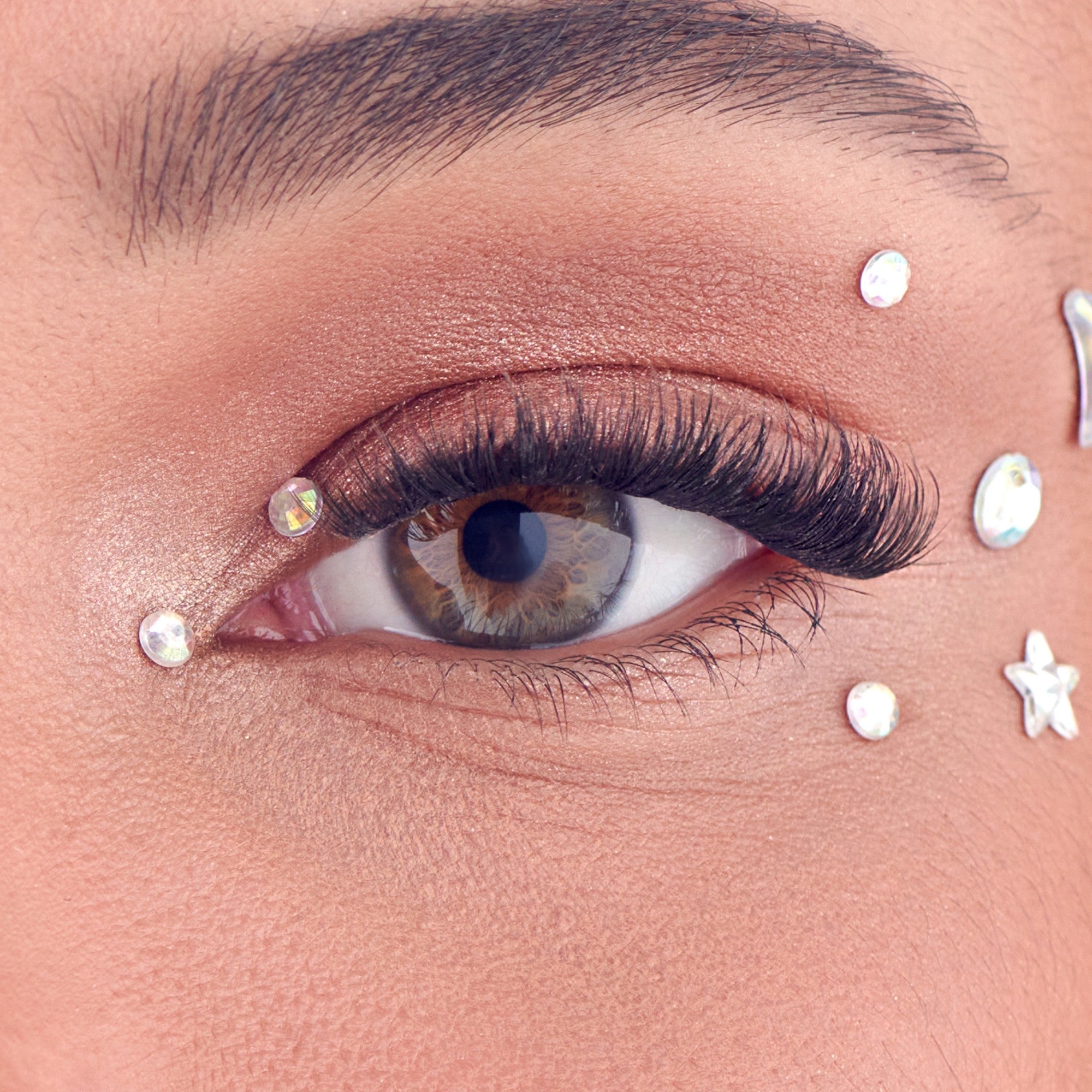 Close-up of eye with dark lashes, warm eyeshadow, and white pearl face gems.