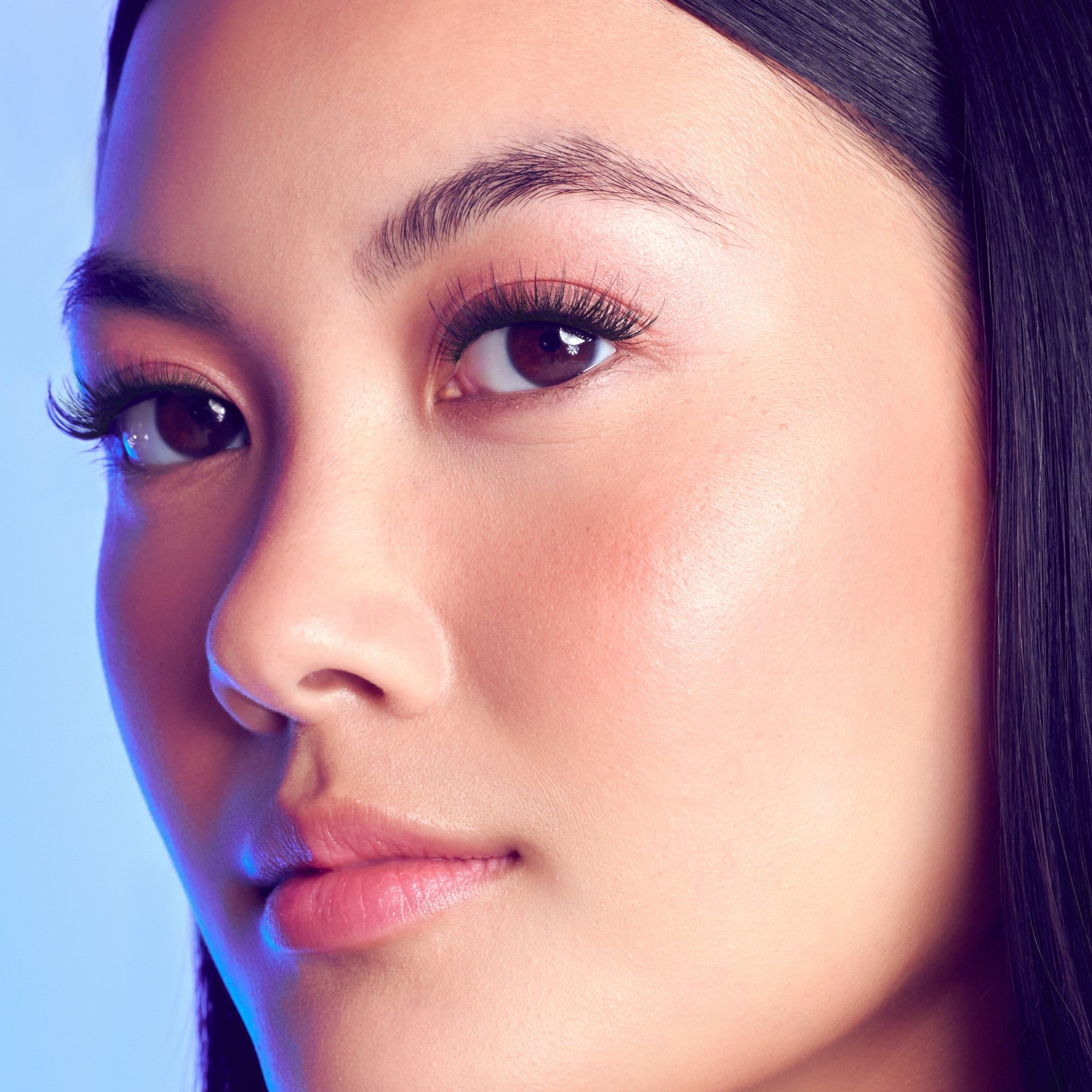 Close-up portrait of woman with dark hair, winged eyeliner, and natural makeup against blue gradient background.