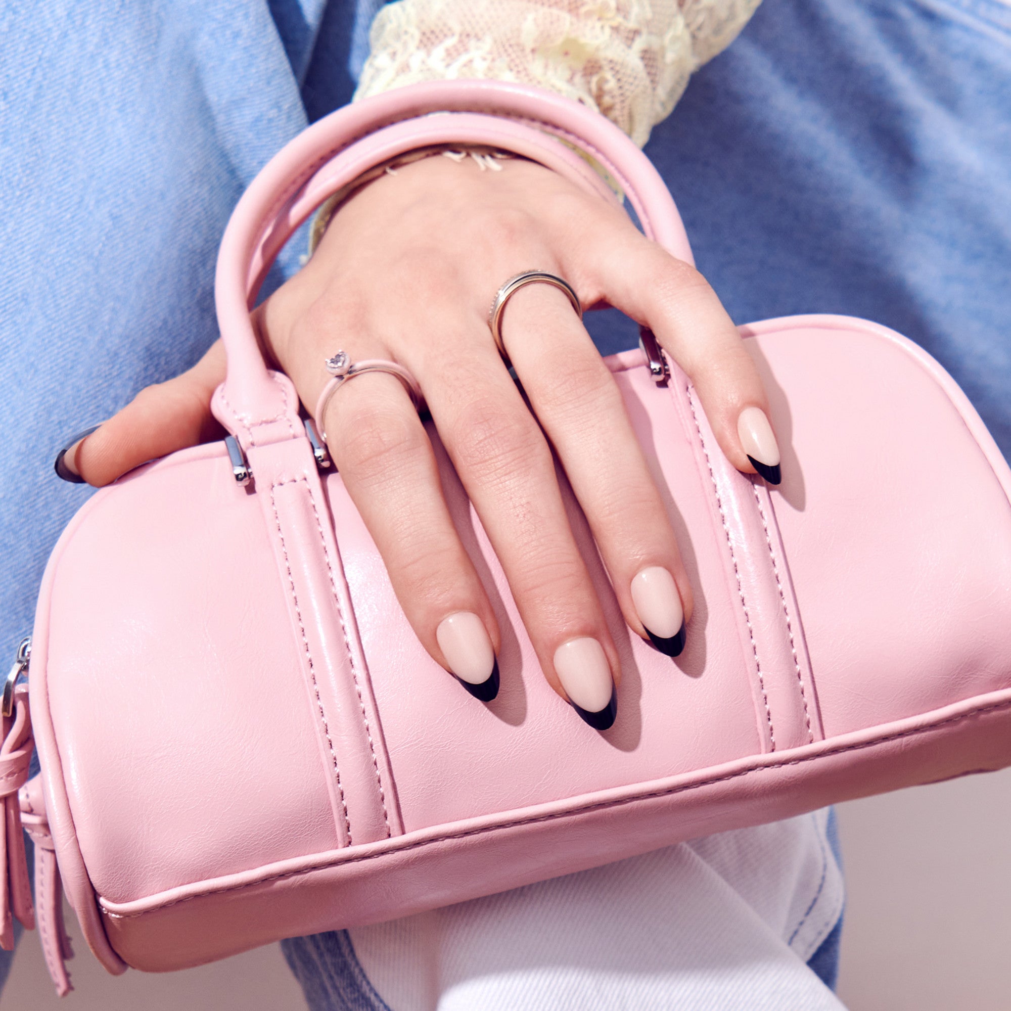 Woman wearing silver rings holding pink leather handbag with black nail art