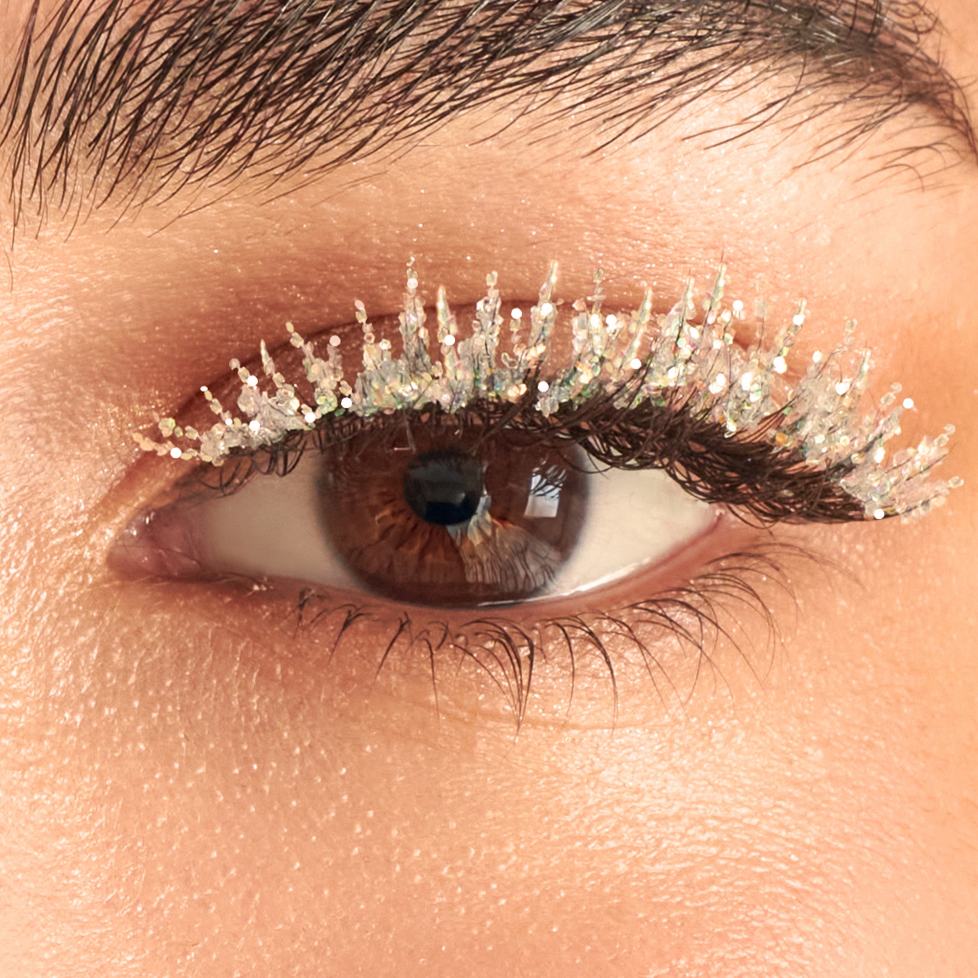 Close-up of eye with glittery silver eyeshadow and dark mascara on warm-toned skin.