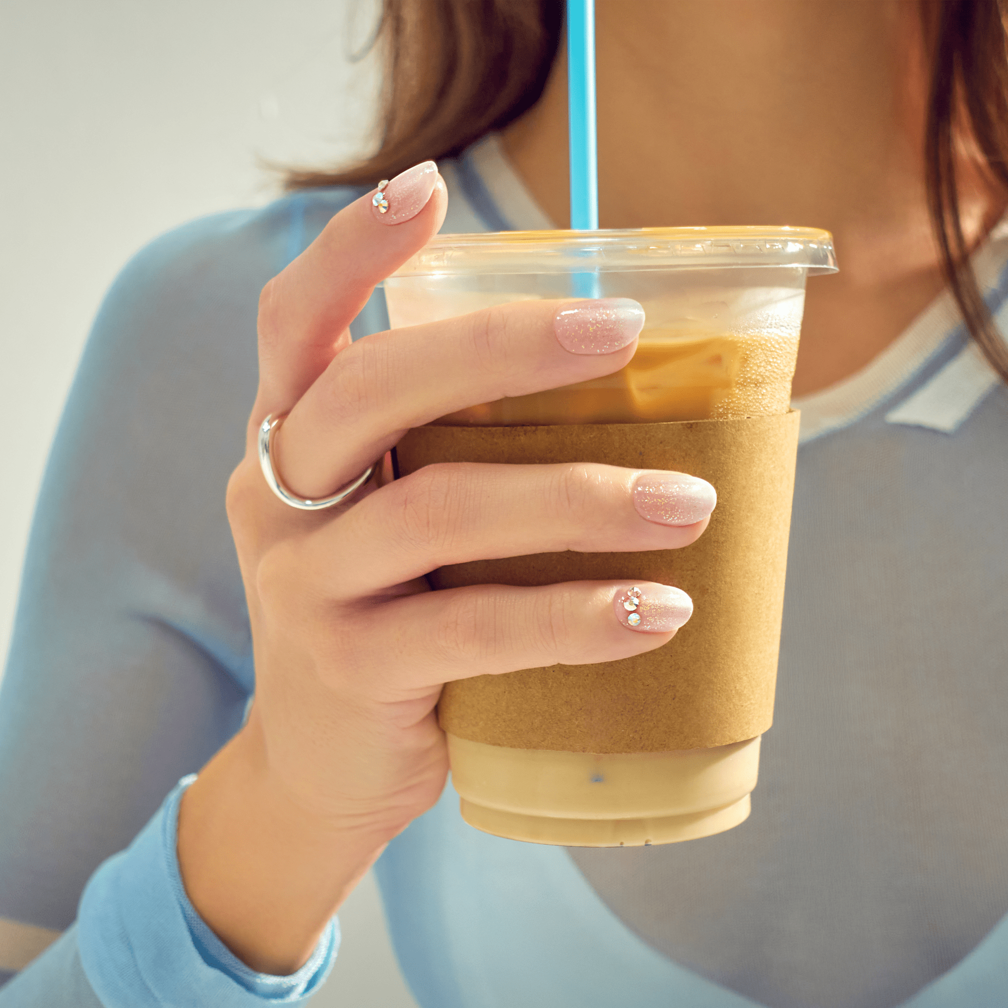 Woman holding iced coffee with manicured nails and ring in sunlight