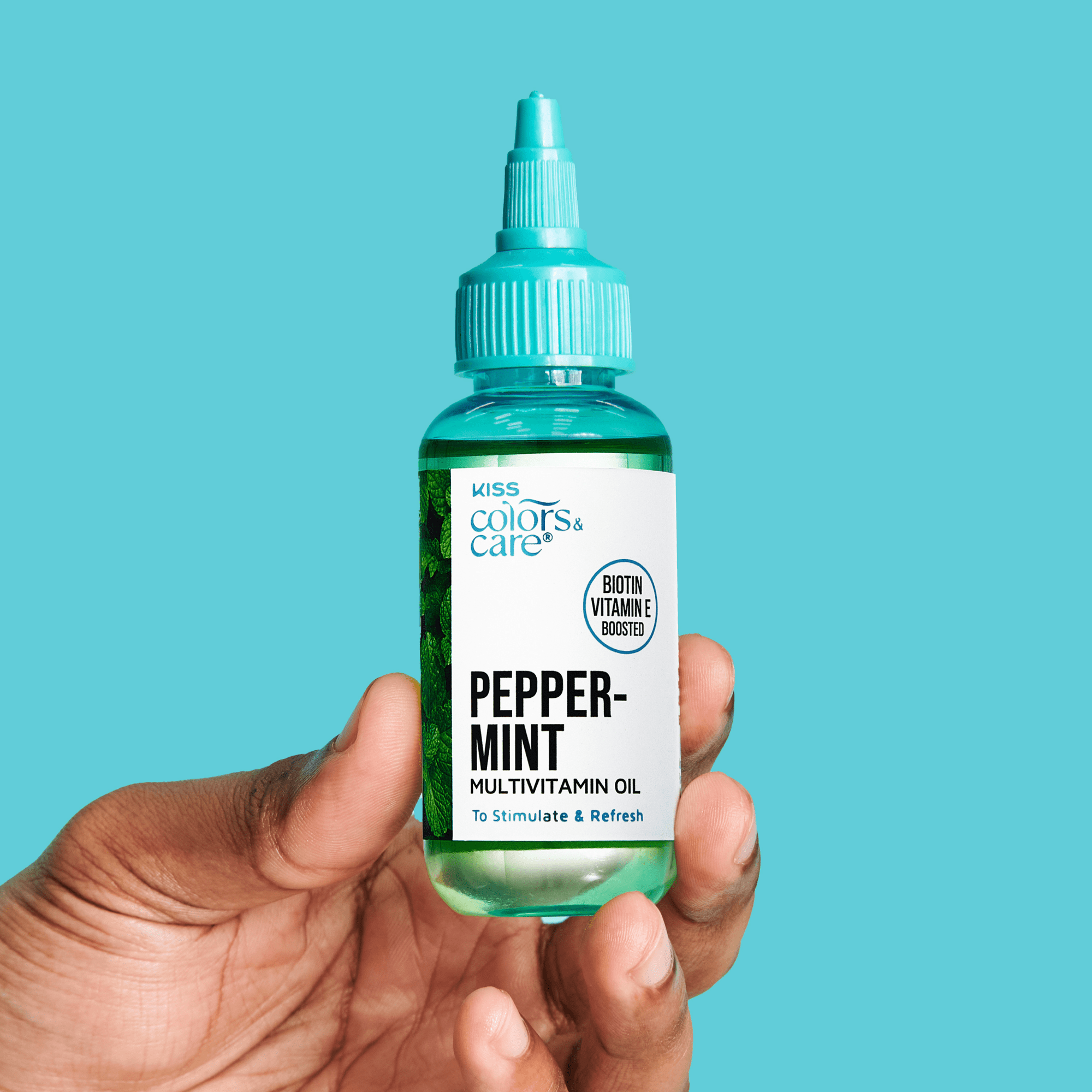 Hand holding a small clear bottle of KISS Colors & Care Peppermint Multivitamin Oil with a turquoise cap, labeled to stimulate and refresh with biotin and vitamin E boost.