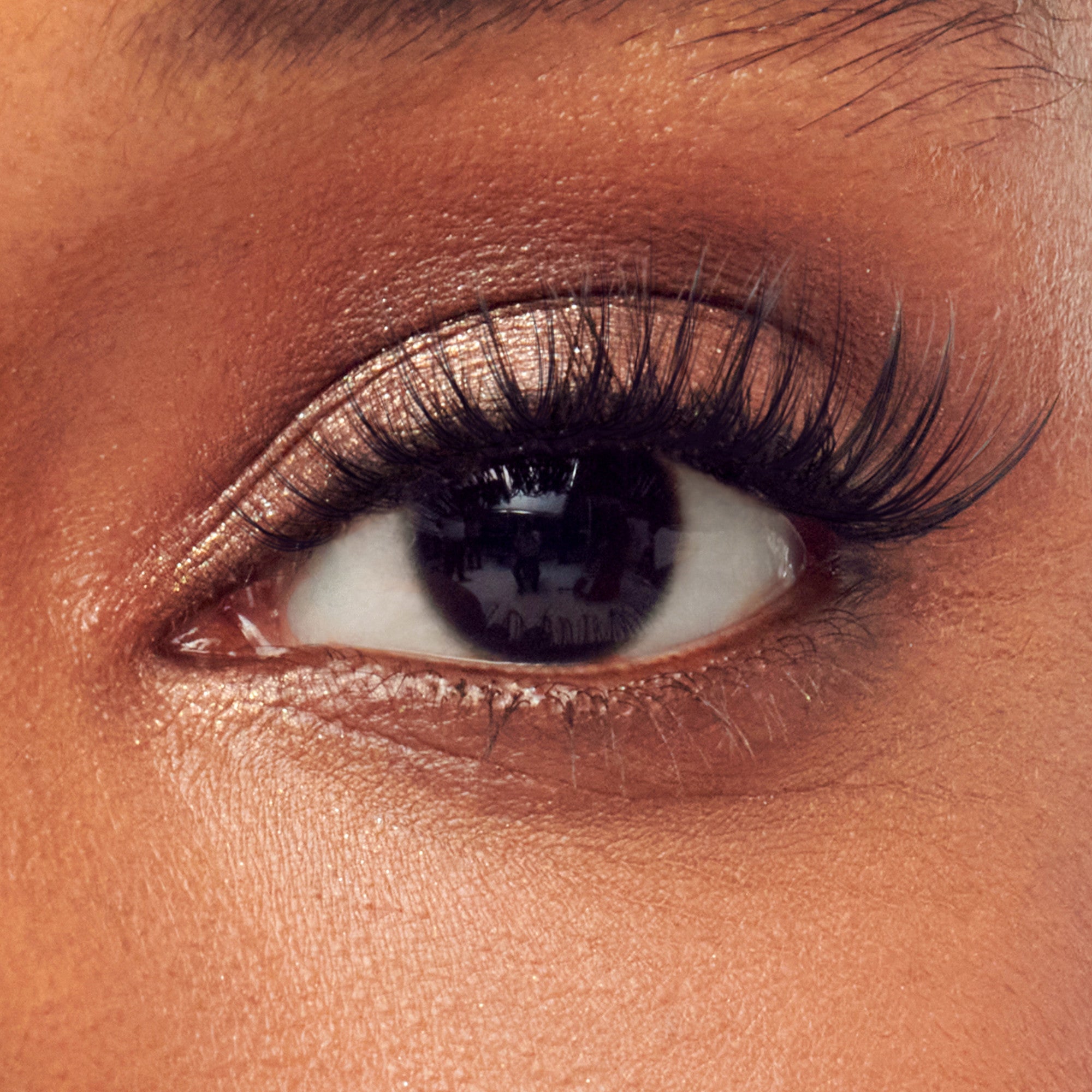 Close-up of eye with bronze eyeshadow, black eyeliner, and volumized black mascara on lashes.