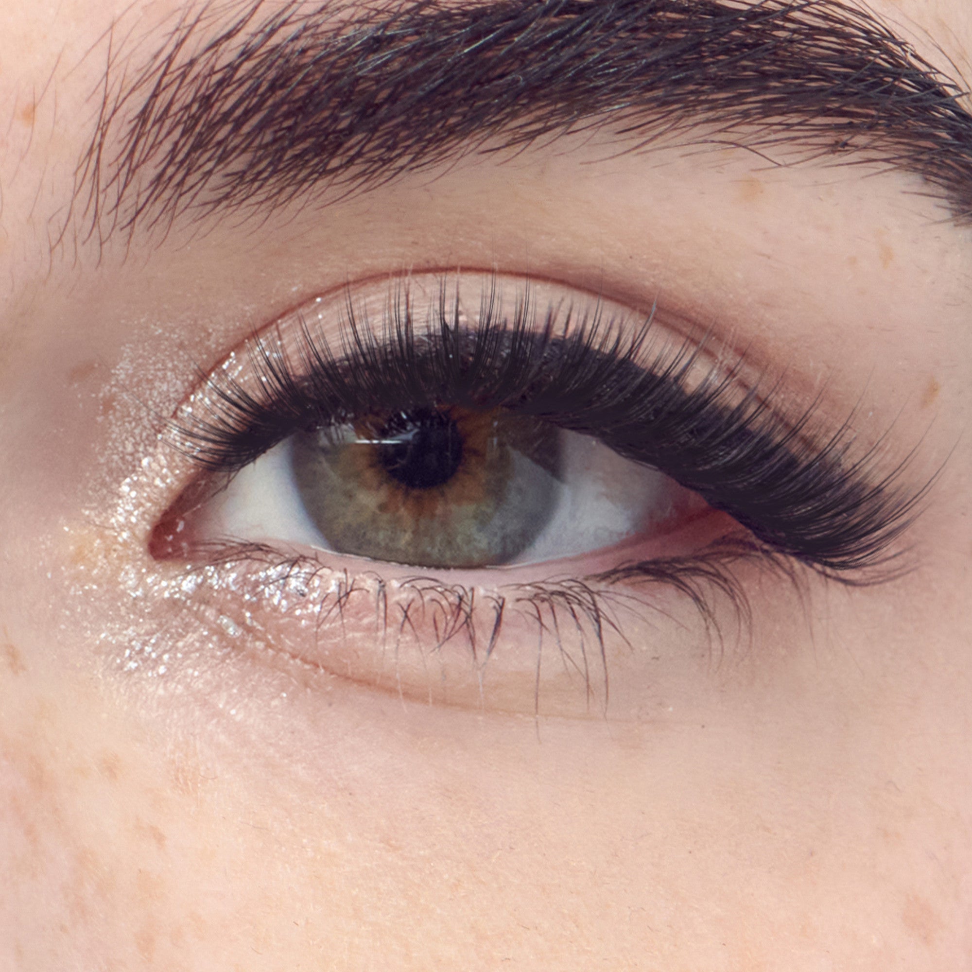 Close-up of a green eye with soft natural-looking thick black press-on adhesive eyelashes applied to the upper lash line.