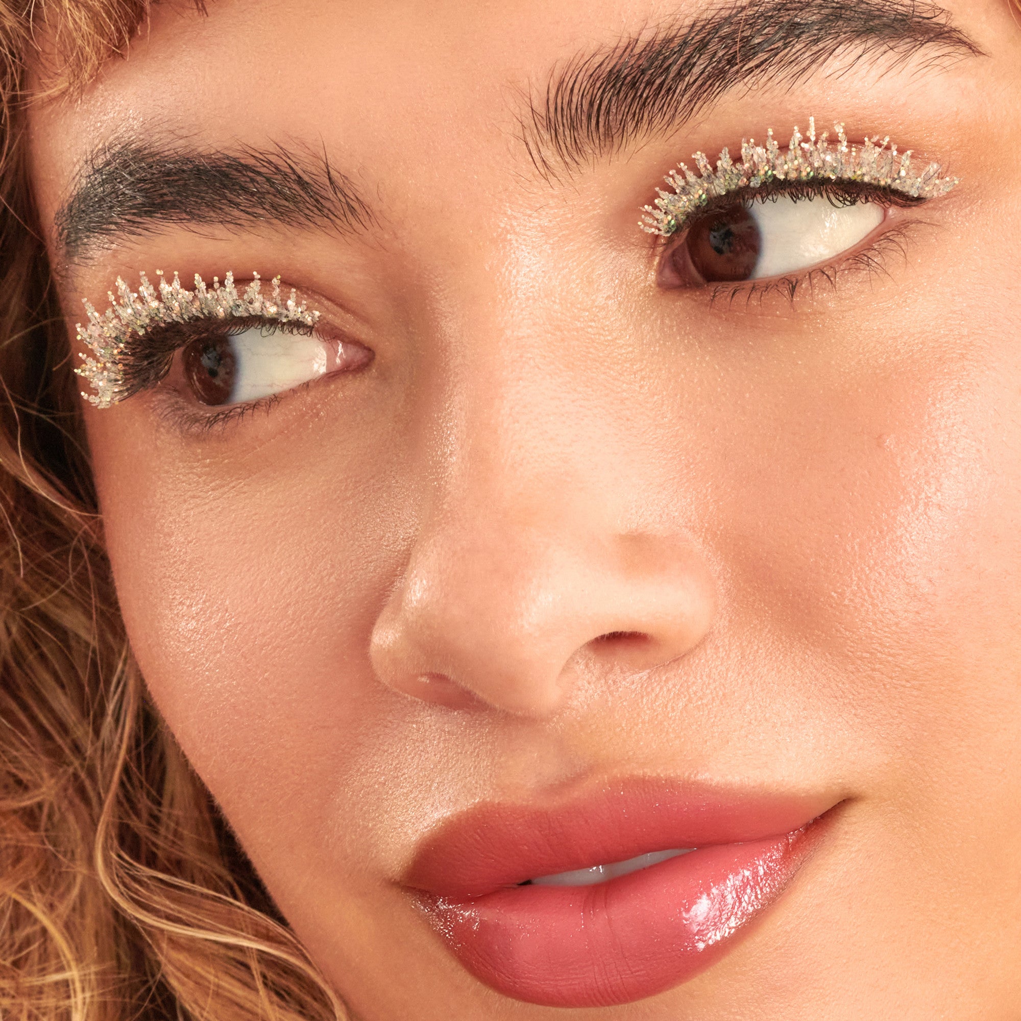 Close-up beauty shot featuring sparkly eyeshadow, defined brows, and coral lipstick.