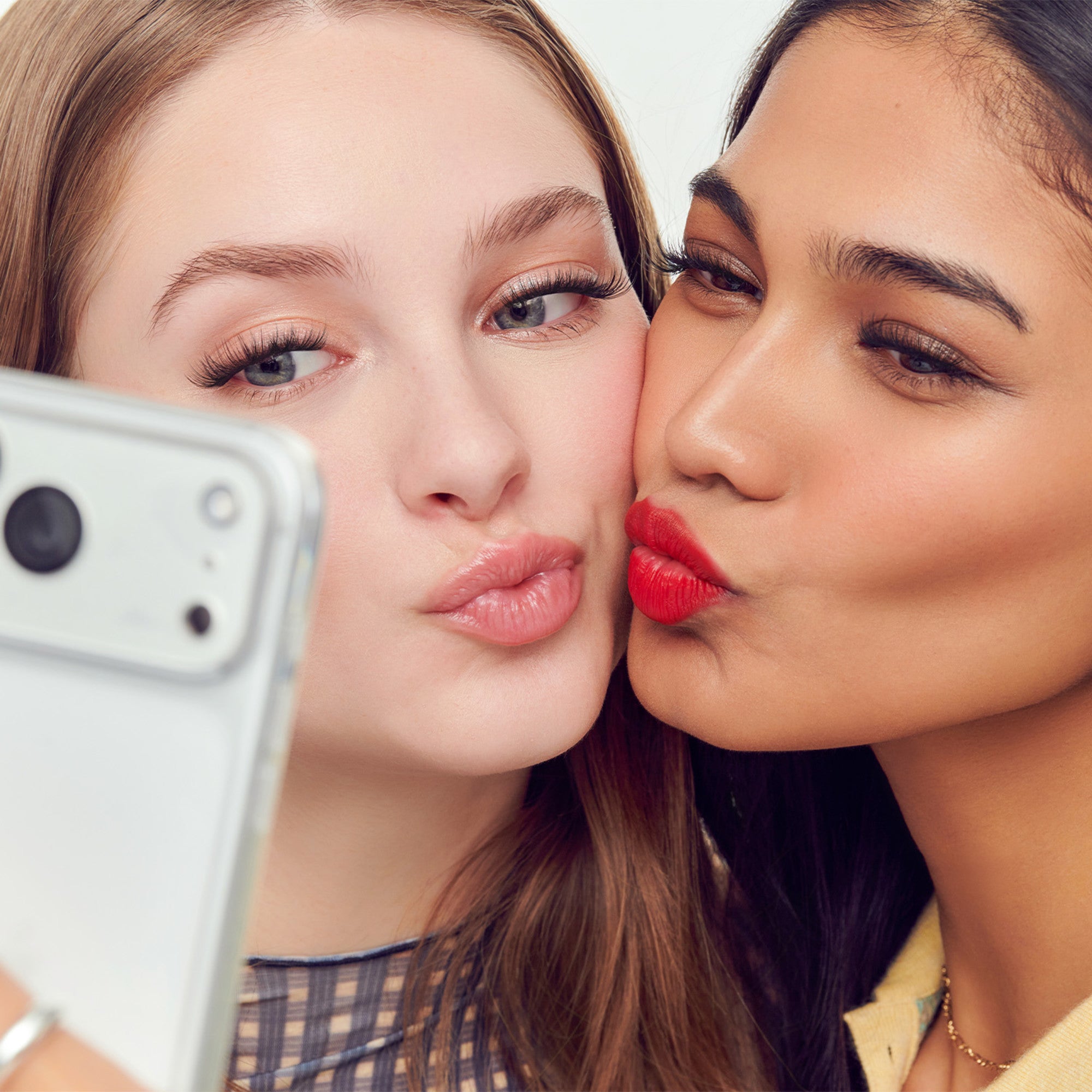 Two women taking a selfie with a white smartphone, making playful expressions.