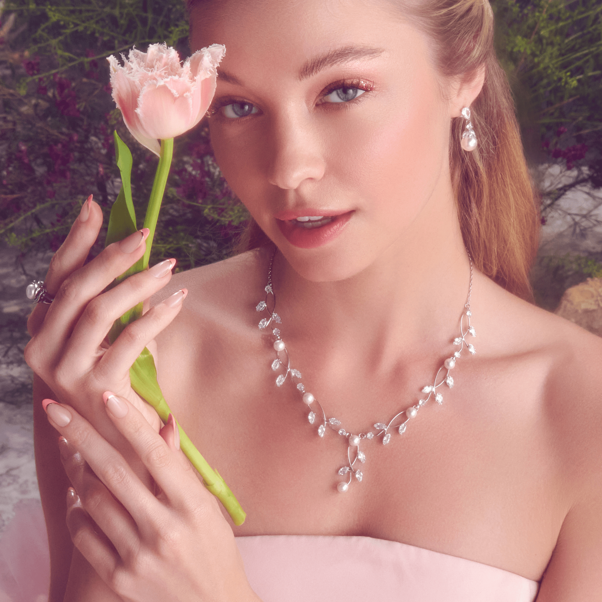 Young woman wearing a silver necklace with pearls and crystal leaves, matching pearl drop earrings, holding a pink fringed tulip in soft natural light.