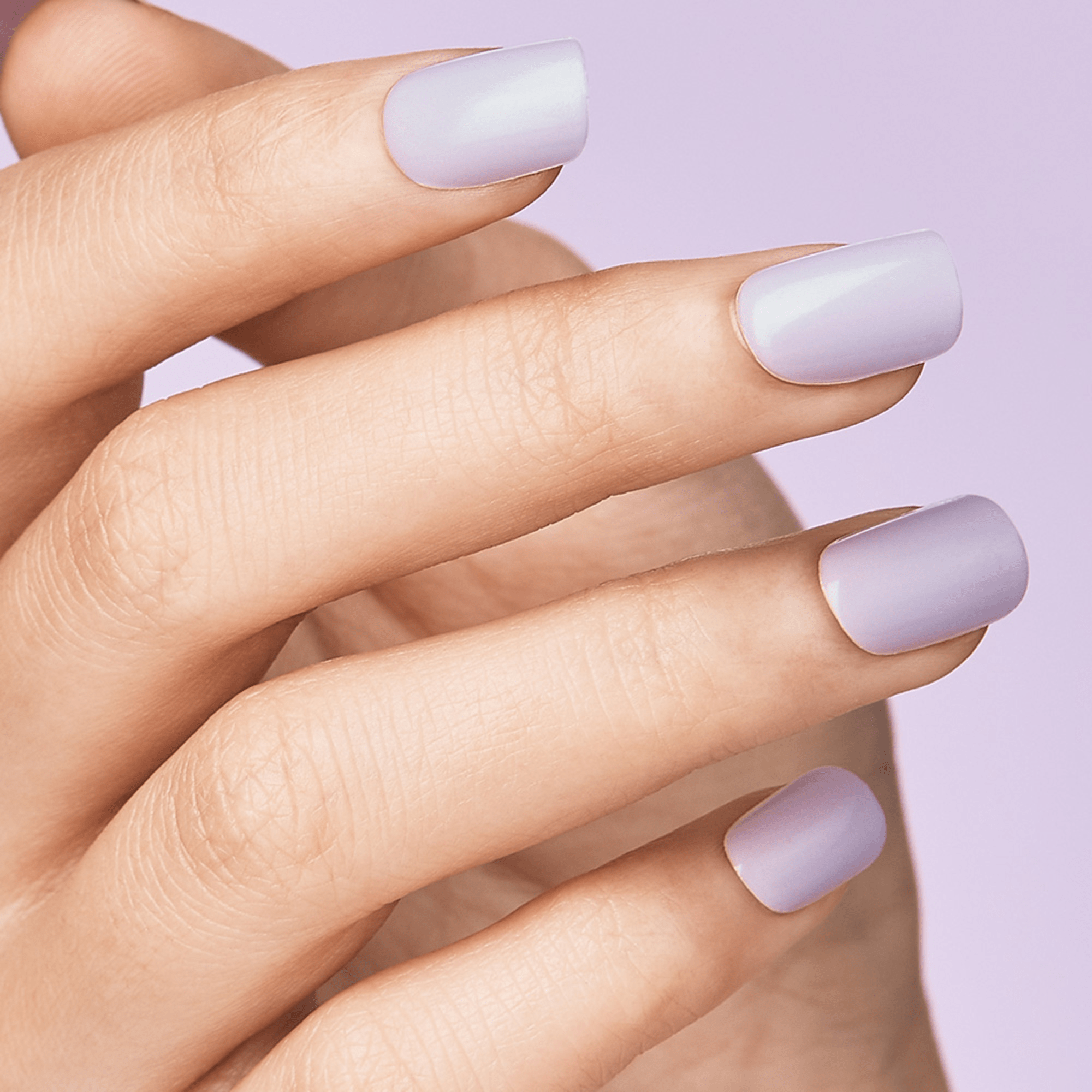 Hand with evenly shaped press-on nails in a soft pastel purple shade against a matching light purple background.
