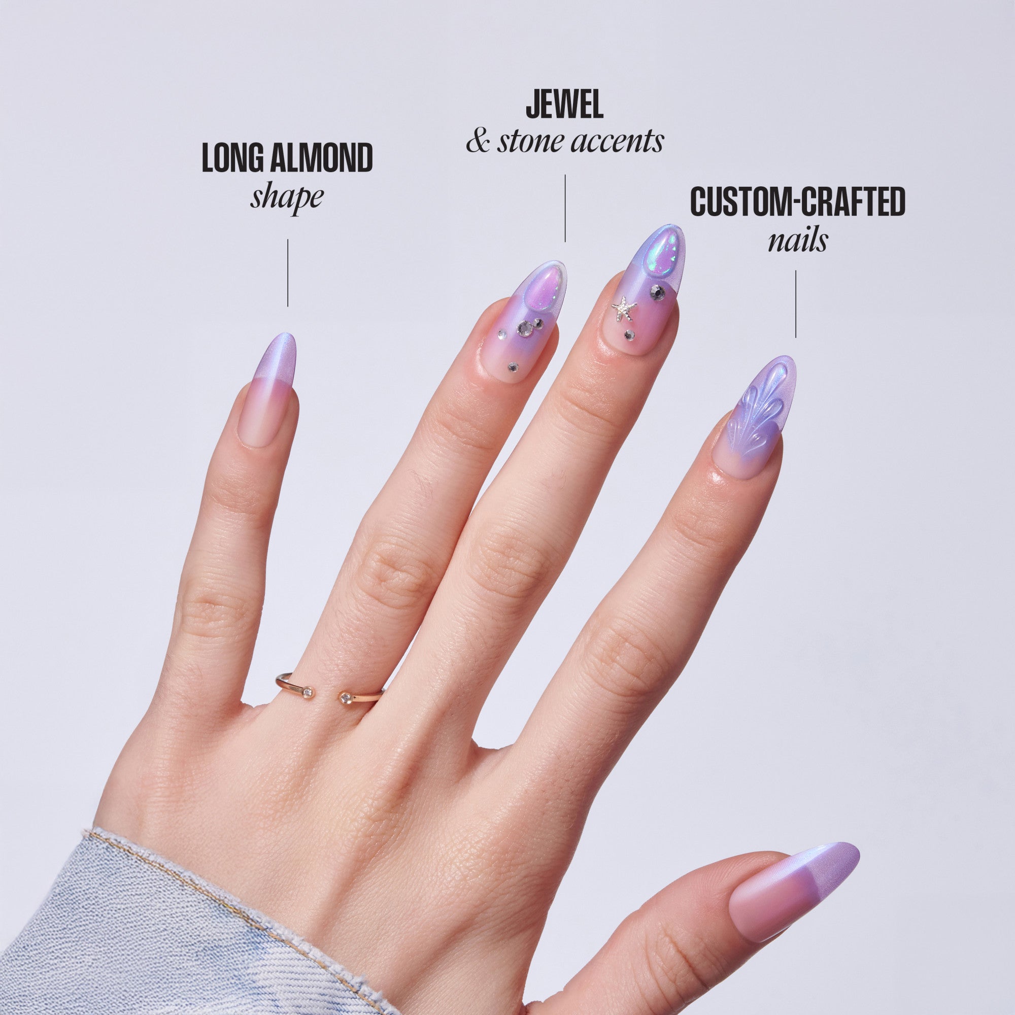 Hand displaying custom nail designs with almond shape, jewels, and stone accents in purple and pink tones.
