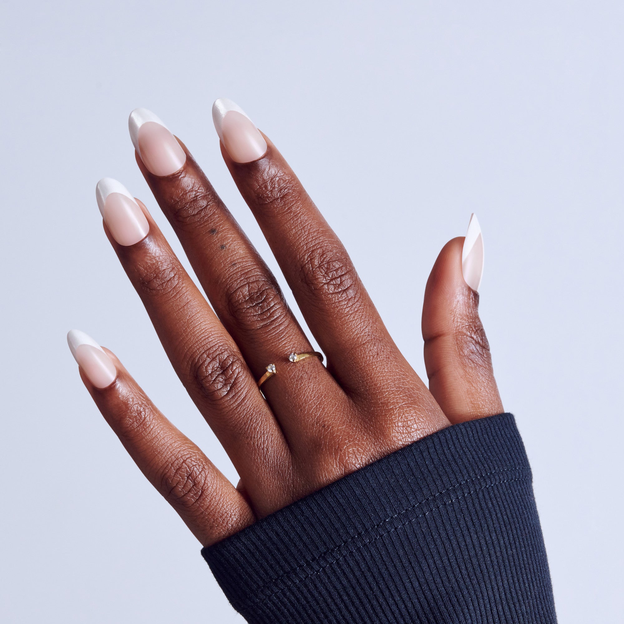 Hand with white French manicure nails and gold rings against light blue background.