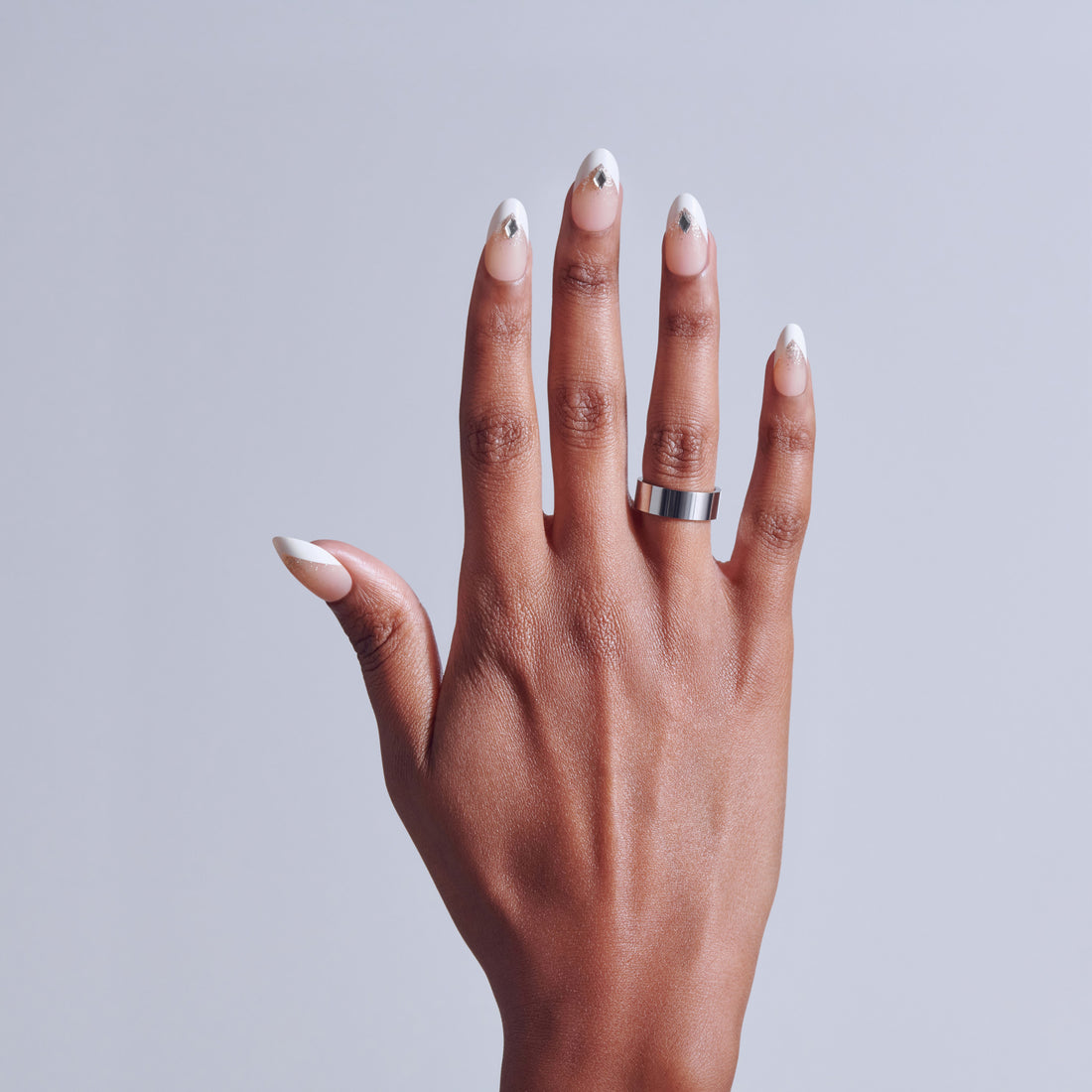 Hand with silver-tipped manicure and metal band ring on light background.