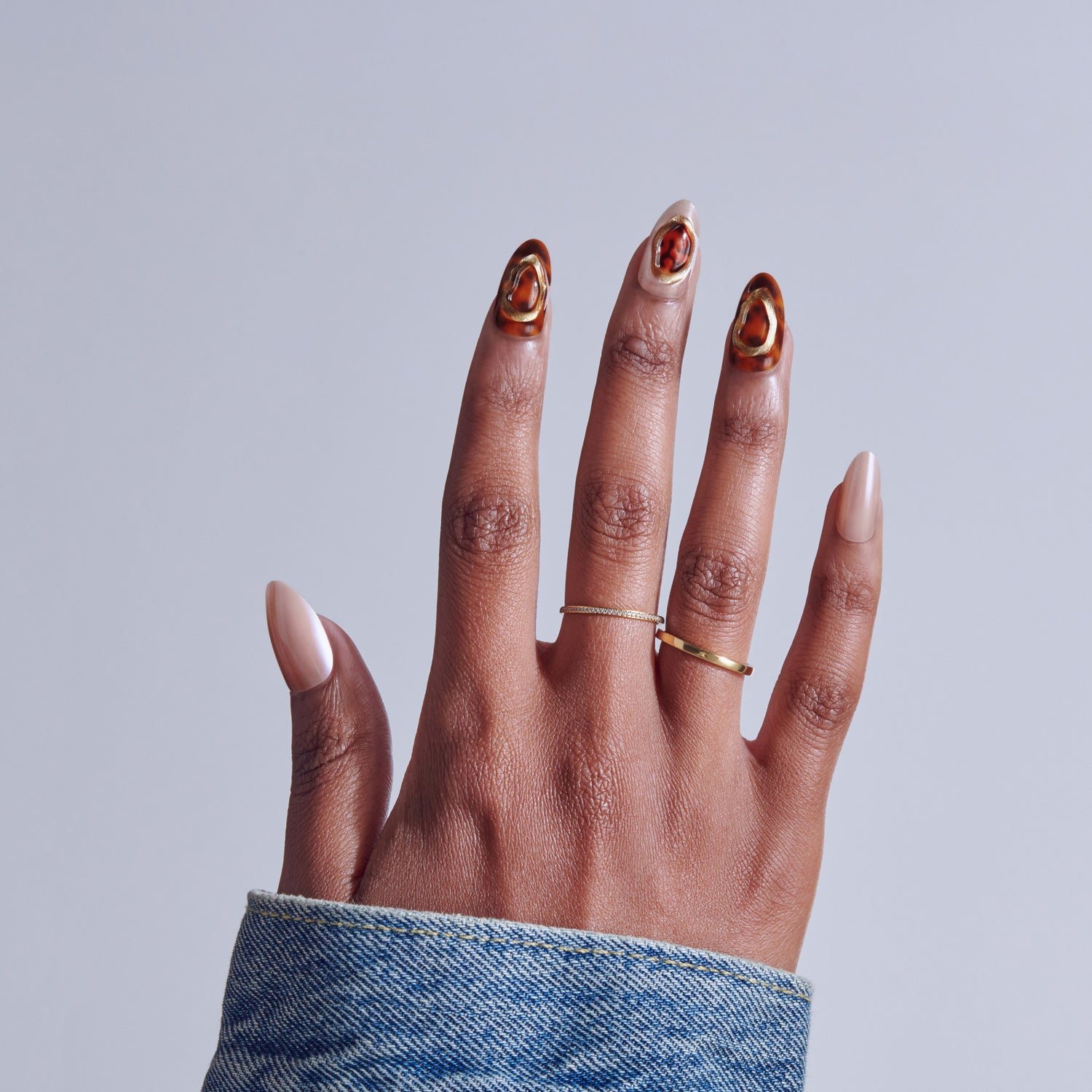 Hand displaying manicure with red and gold nail art and gold rings against gray background.