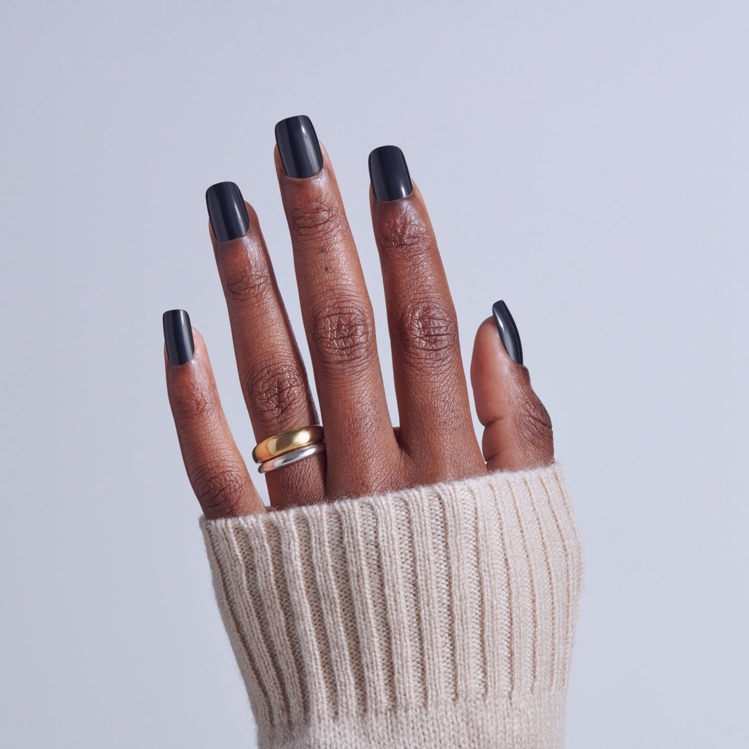Hand with black ombre nails and gold ring, wearing cream ribbed sweater.
