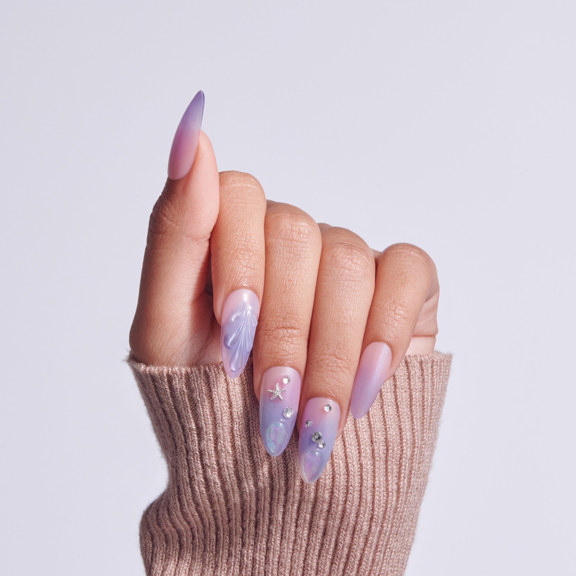 Almond-shaped nails with purple ombre gradient and rhinestone embellishments on hand in beige sweater.
