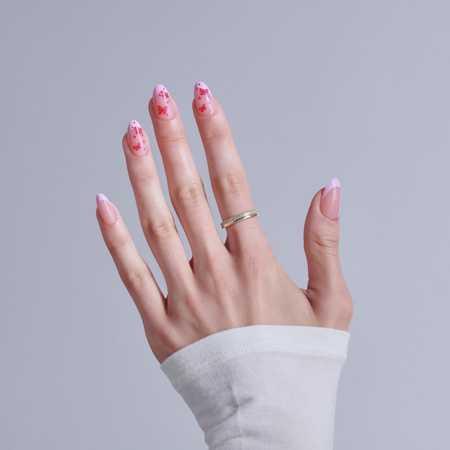 Hand displaying pink butterfly nail art with diamond ring on white sleeve background