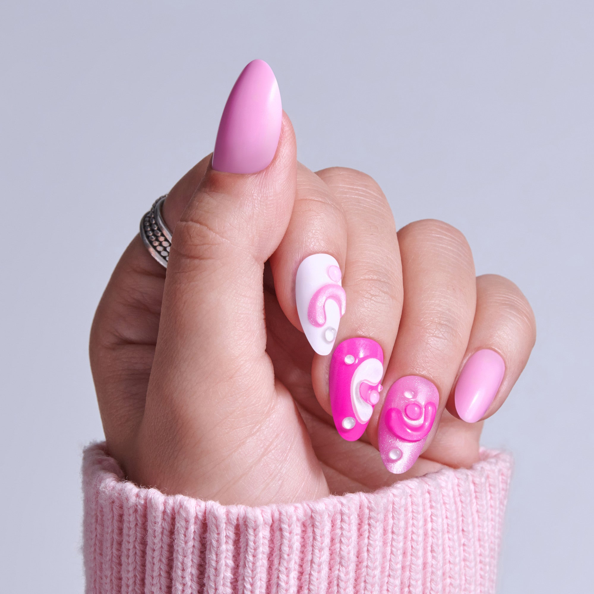Pink manicure with almond nails featuring white and hot pink swirl designs on hand in pink sweater.