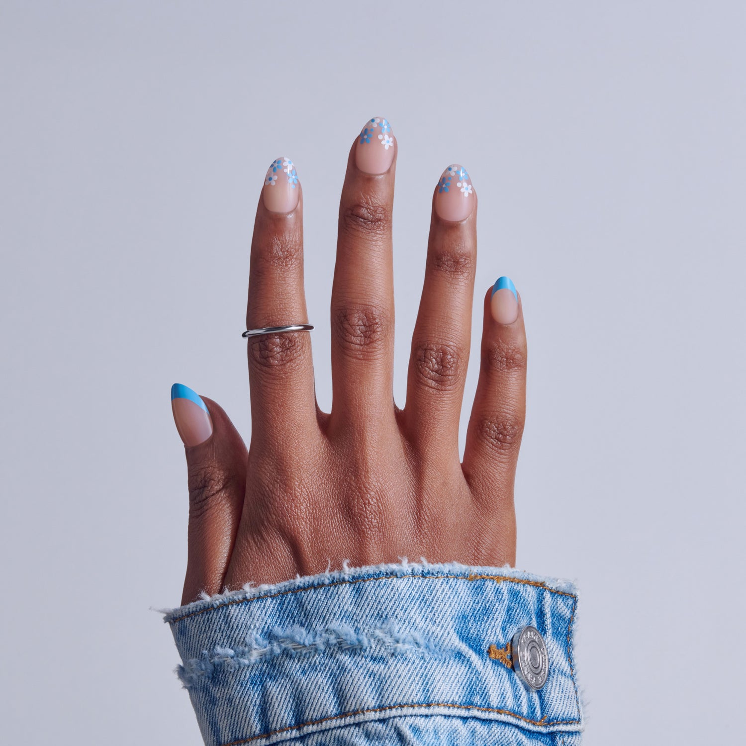 Hand with blue and white snowflake nail art and silver ring, wearing denim cuff.