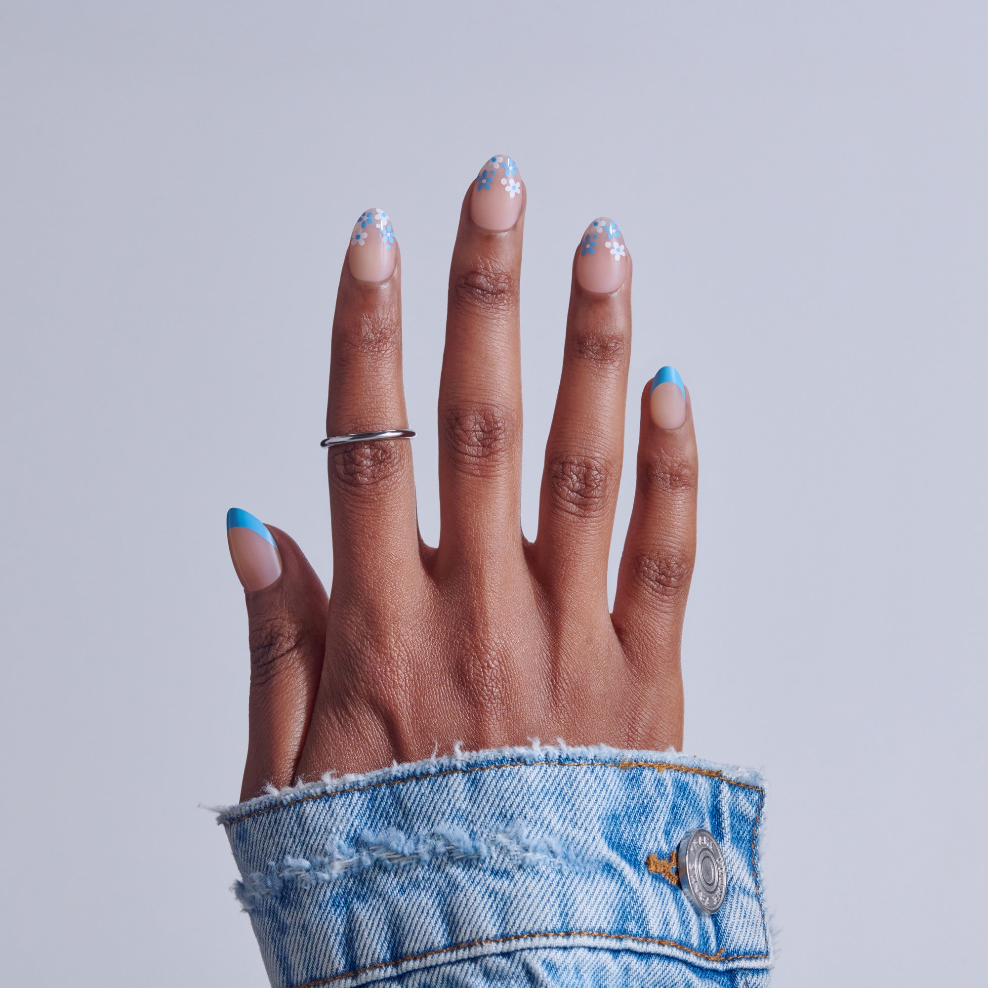 Hand with blue and white snowflake nail art and silver ring, wearing denim cuff.