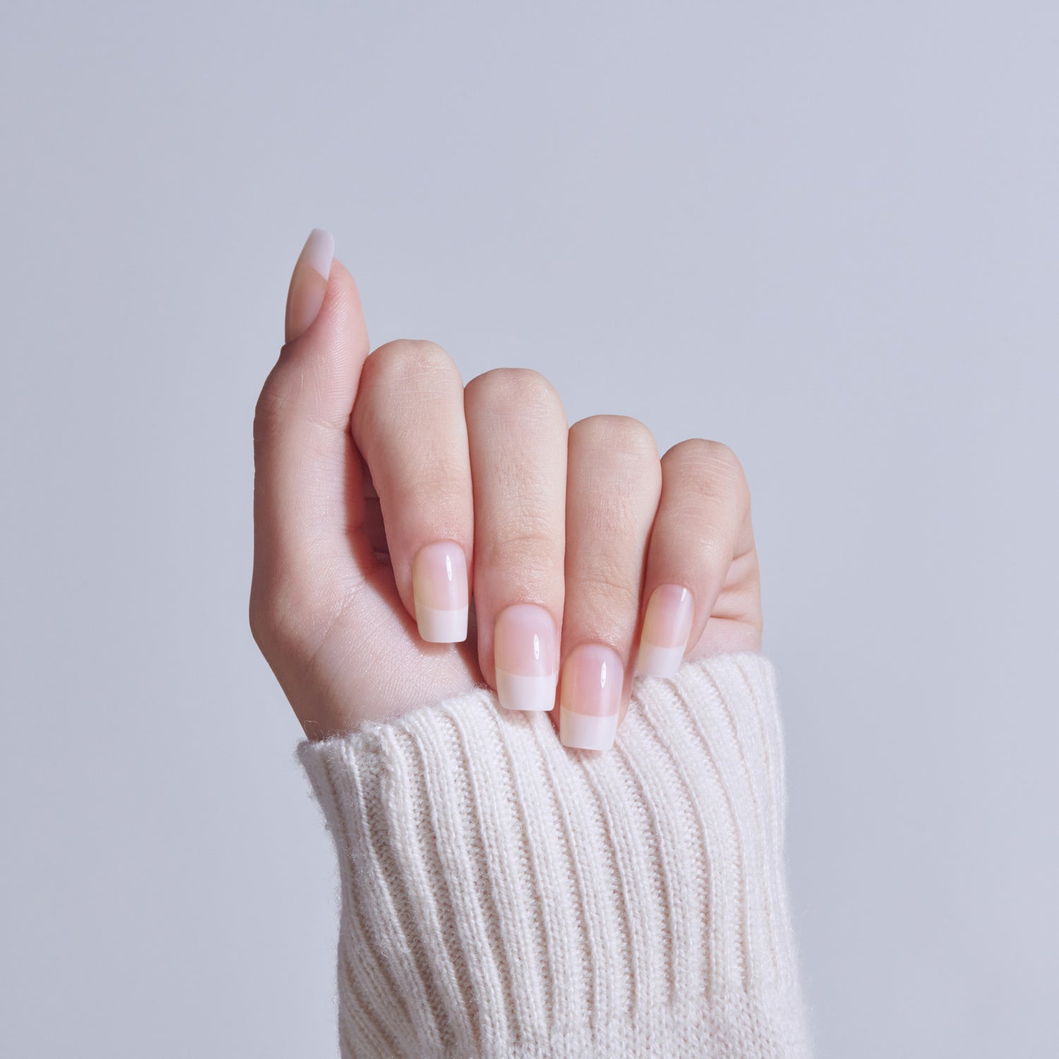 Manicured nails with soft pink and white ombre nail polish design on outstretched hand.