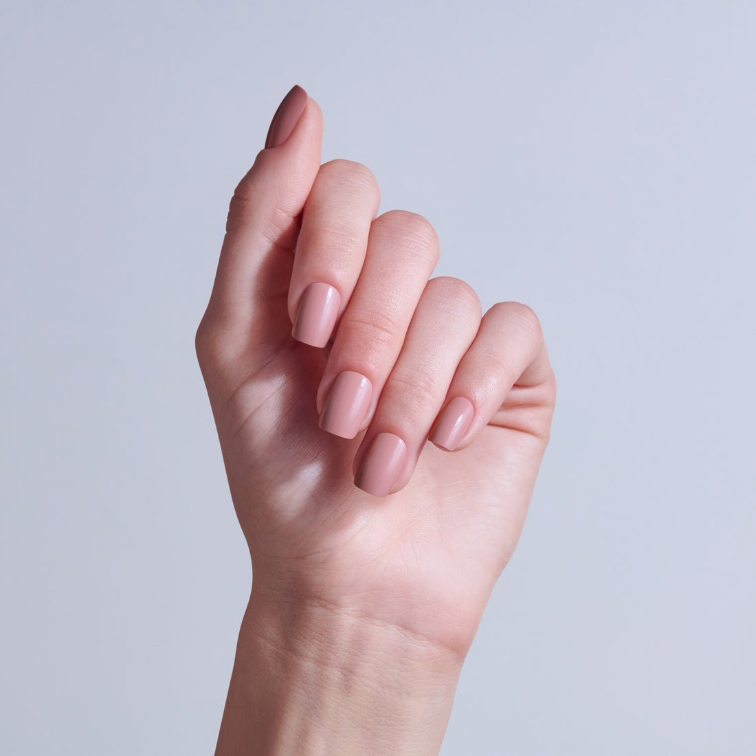 Hand displaying manicured nails with soft pink nail polish against light background.