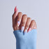 Hand with manicured nails featuring pink ombre, floral designs, and almond shapes against blue sleeve.