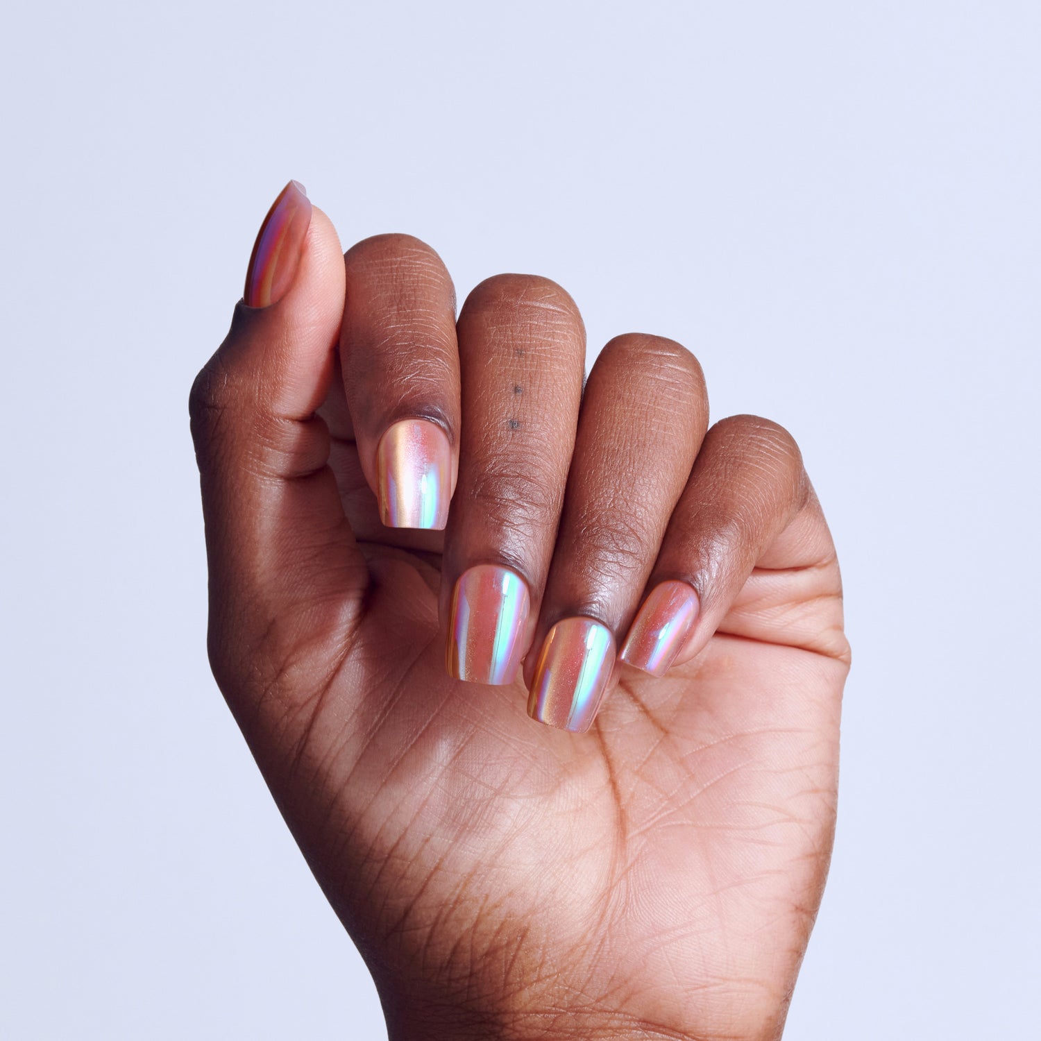 Hand displaying holographic nail polish manicure on short, rounded nails against light background.