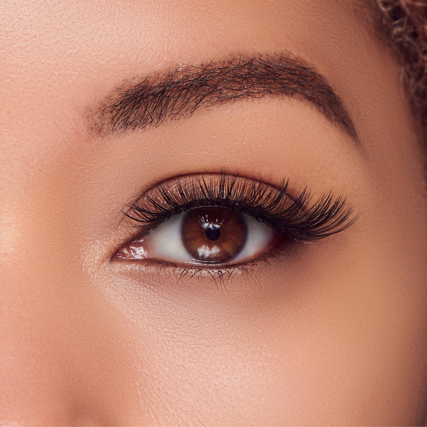 The image features a close-up of a human eye, showcasing a rich brown iris. The eyelashes are long and voluminous, enhancing the eye&