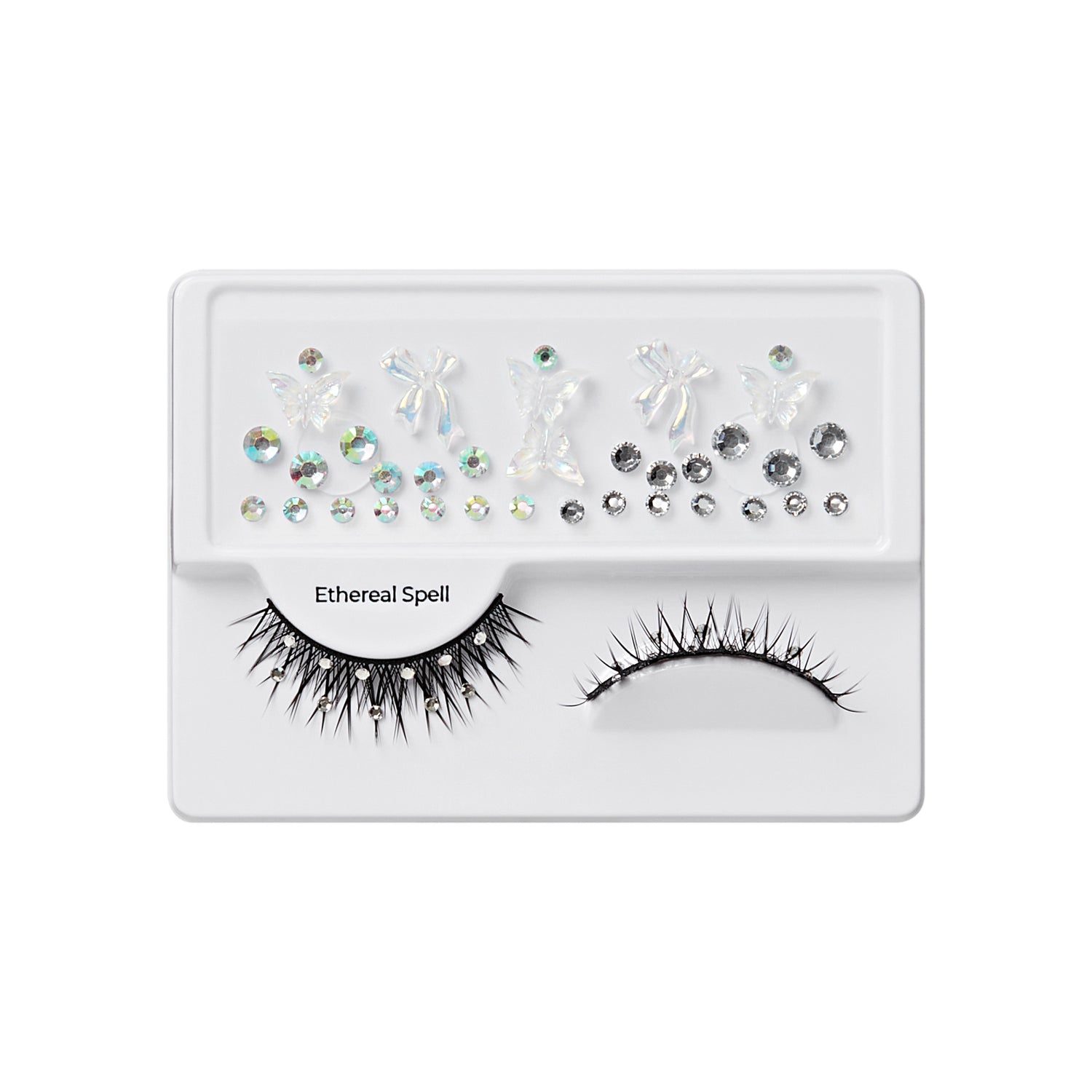 The image features a makeup product display, specifically a set of false eyelashes and decorative embellishments. The packaging is white and includes two pairs of eyelashes: one with long, spiky strands and another with a more natural look. Above the eyelashes, there are various decorative elements, including small rhinestones and shapes that resemble butterflies and other designs, all in different sizes and finishes. The set is labeled "Ethereal Spell," suggesting a whimsical or magical theme.