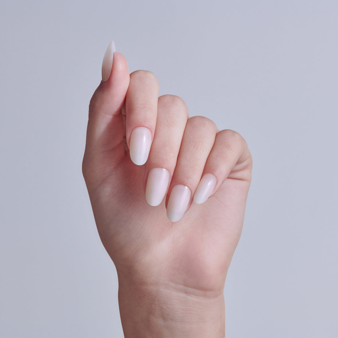 Hand displaying almond-shaped nails with soft pink and white ombre nail polish manicure.