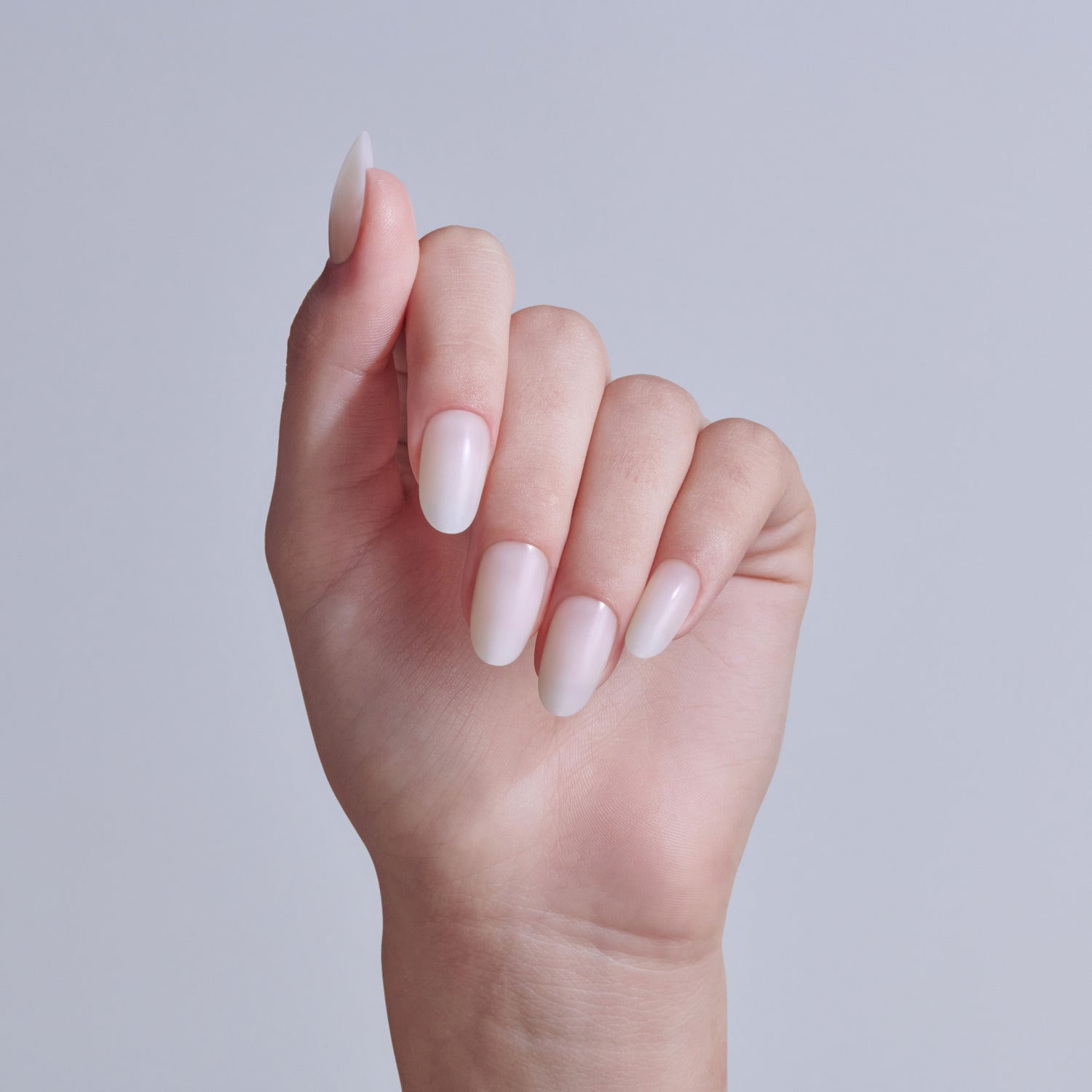 Hand displaying almond-shaped nails with soft pink and white ombre nail polish manicure.