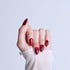 Hand with deep red metallic almond-shaped nails against light blue background