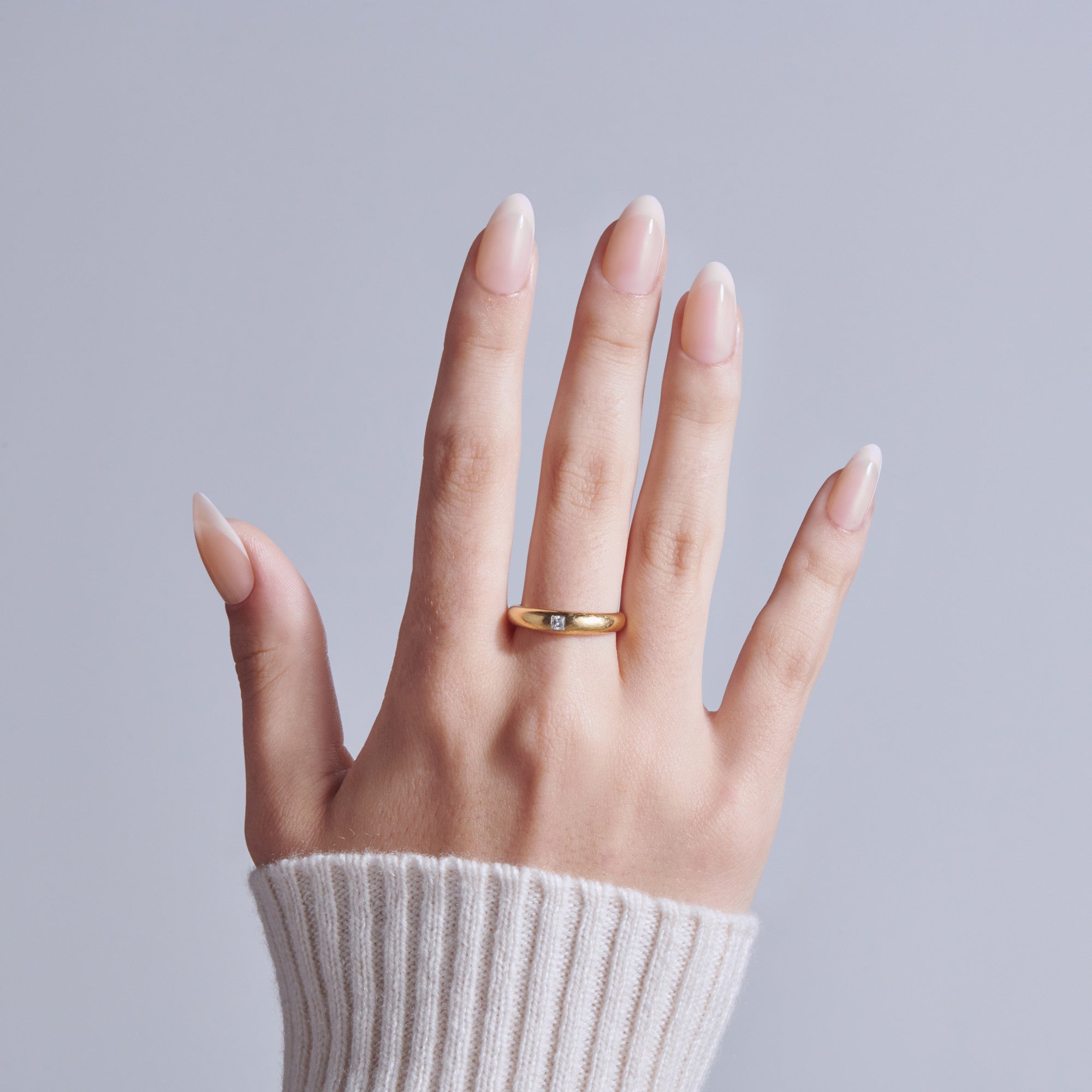 Hand wearing gold wedding band with natural almond-shaped nails and white sweater