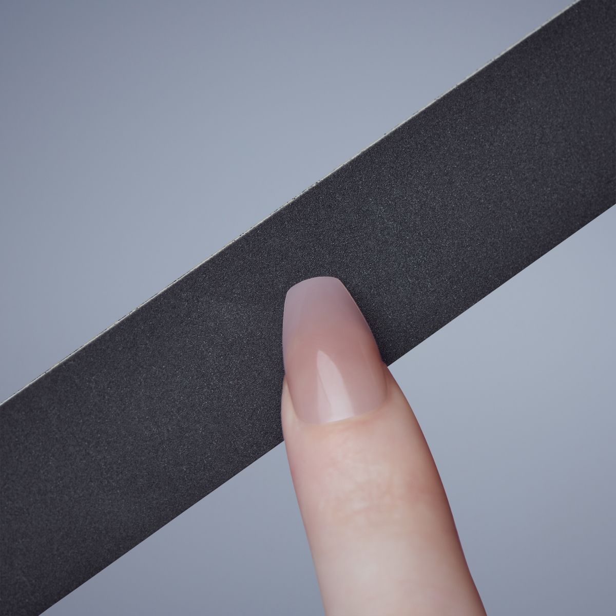 Close-up of a hand holding a black rectangular nail file against a gray background, showing the smooth surface and a manicured fingertip.