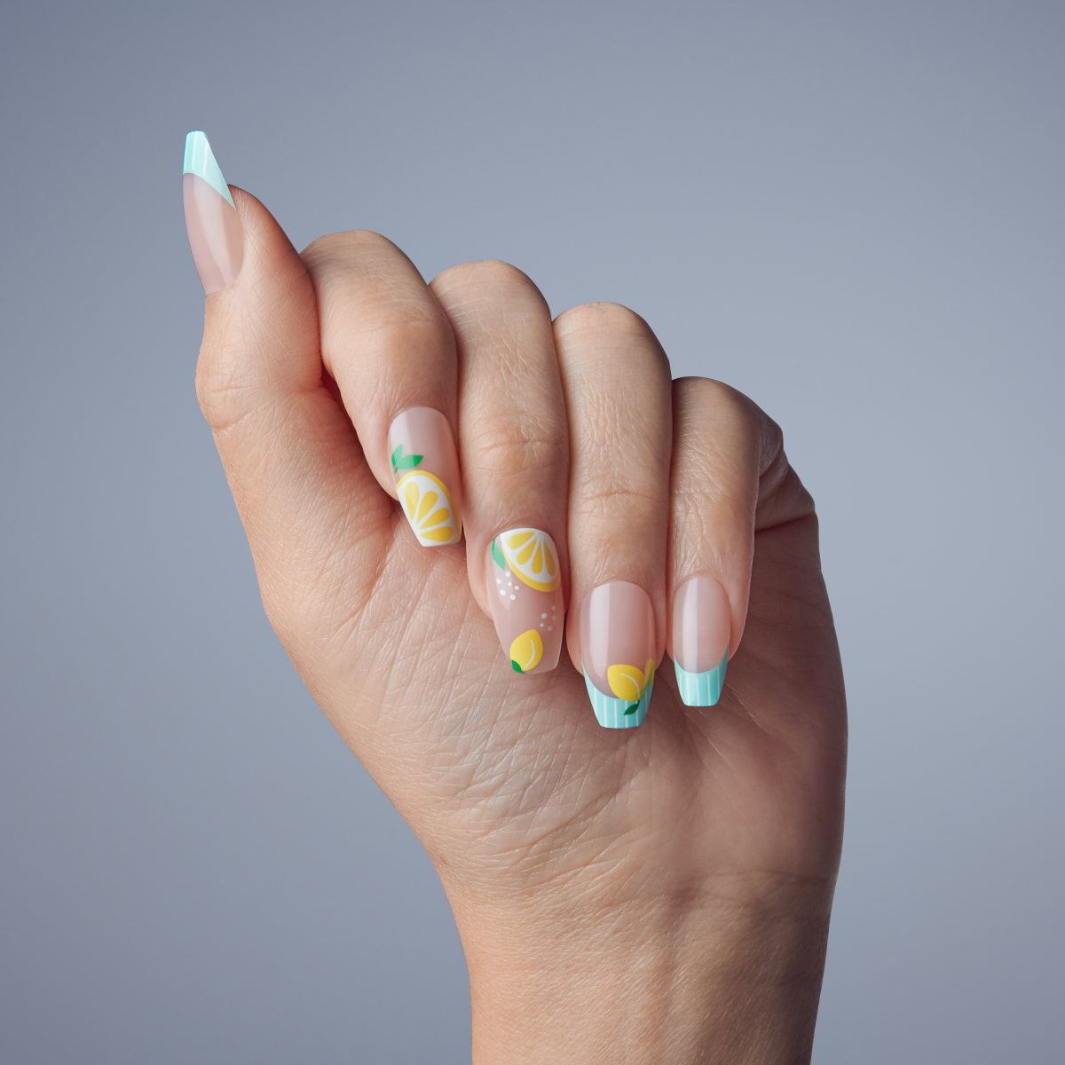 Hand with medium-length nails featuring pastel blue French tips and lemon-themed nail art on a light gray background.