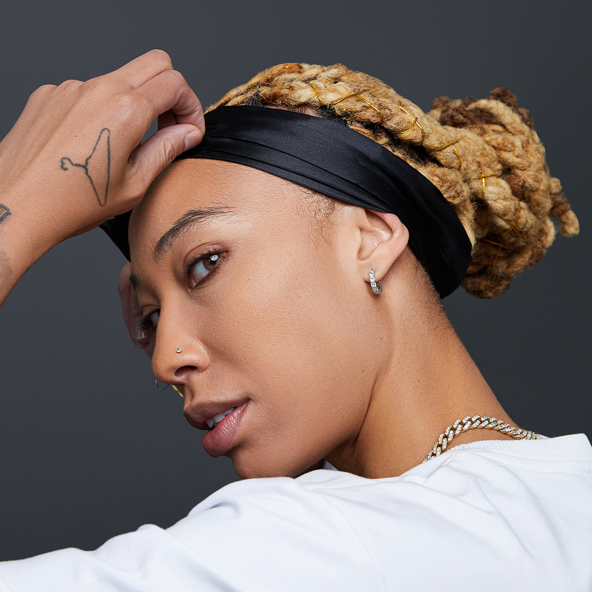 Person with light brown braided hair tied back, wearing a smooth black satin edge scarf across the forehead, shown in close-up from the side.