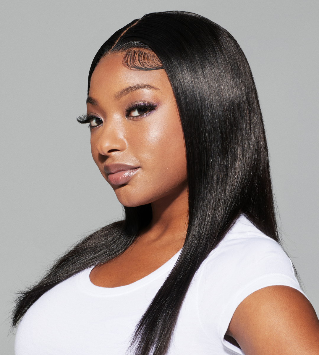Young woman with long, sleek, straight black hair styled with defined baby hairs, wearing a white t-shirt, against a plain gray background.