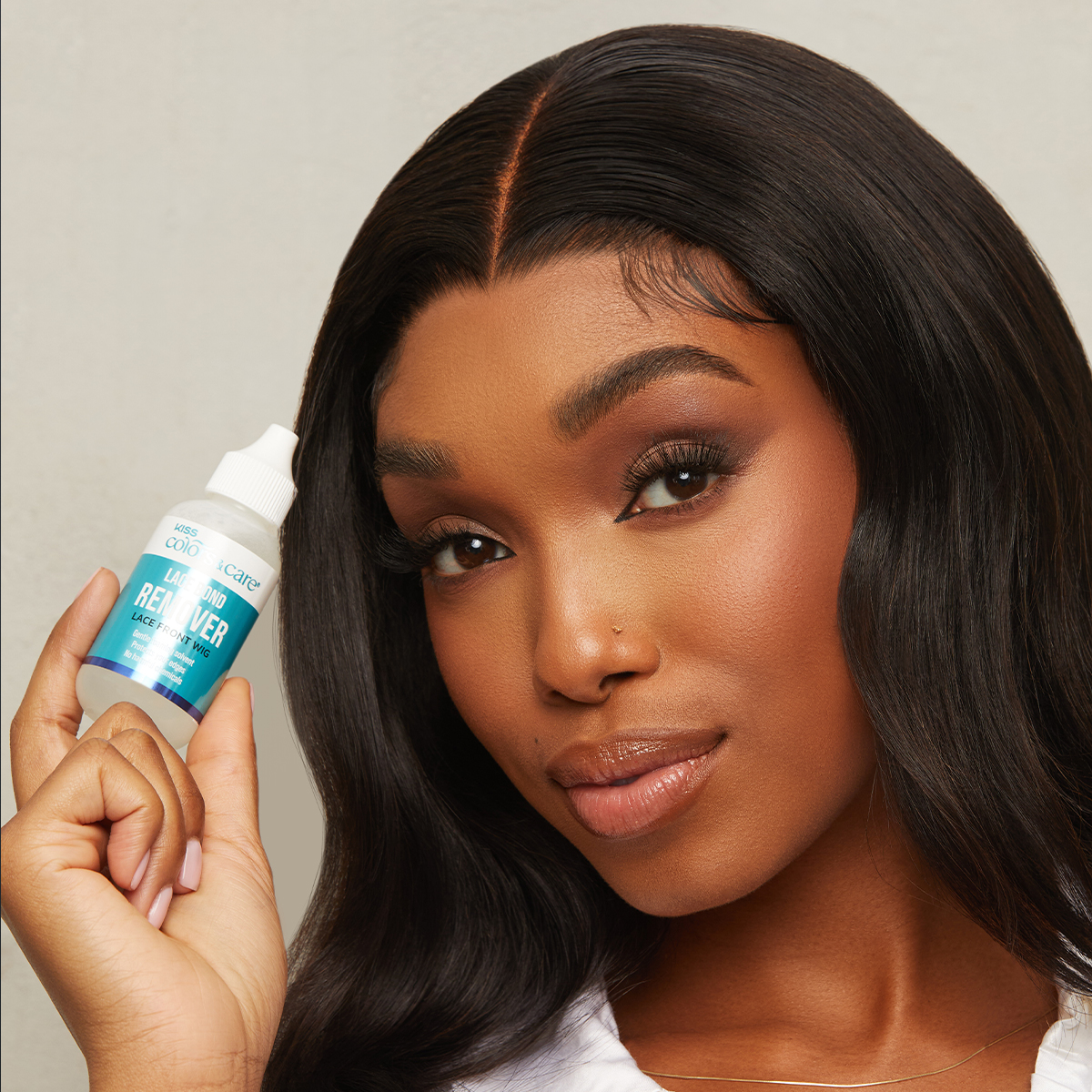 Woman with smooth, styled dark hair holds a small bottle of KISS Colors &amp; Care Lace Bond Remover, labeled for lace front wigs, gentle and no harsh chemicals.
