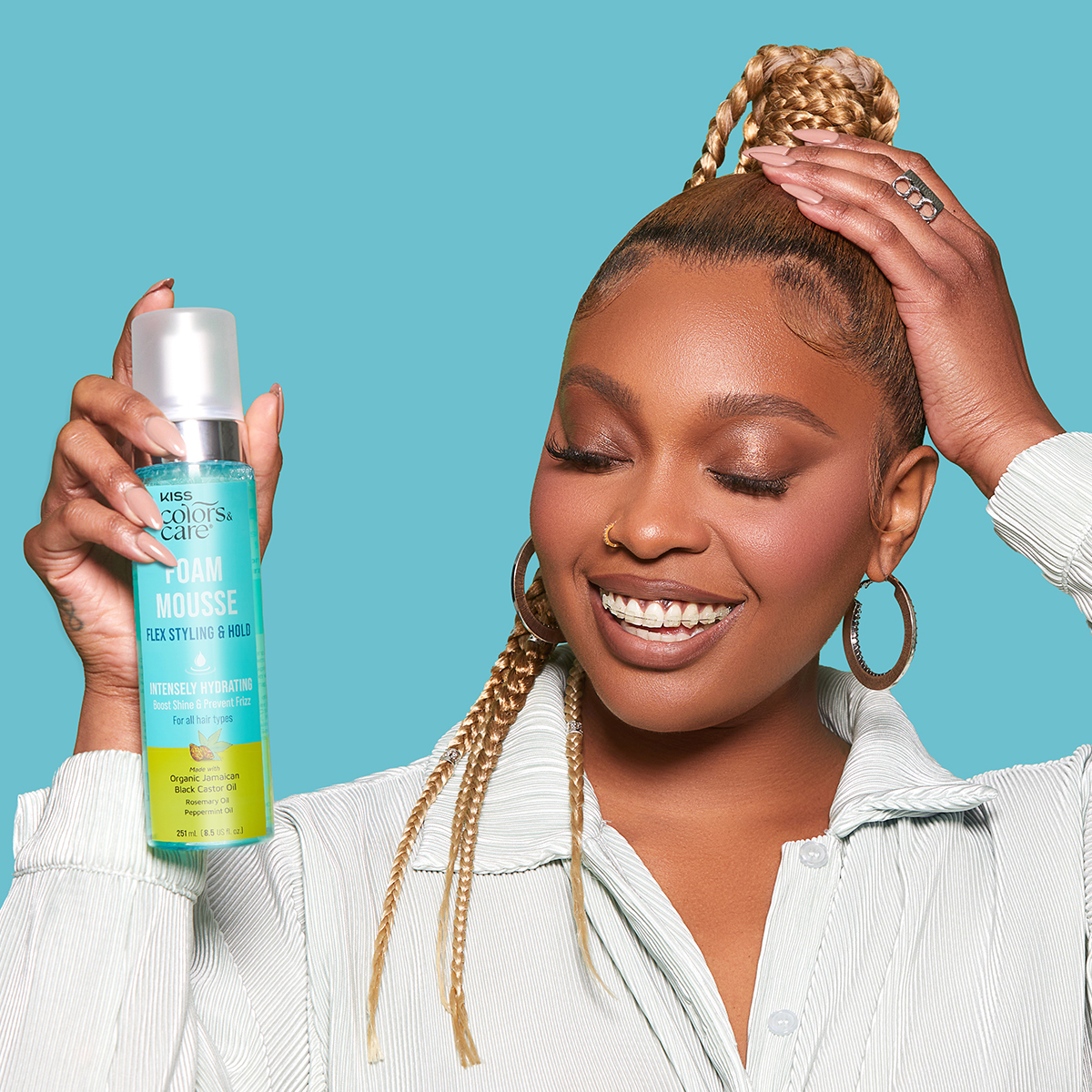 Smiling woman with braided blonde hair holds a blue and yellow bottle of KISS Colors &amp; Care Foam Mousse that highlights flex styling, intense hydration, and frizz prevention.