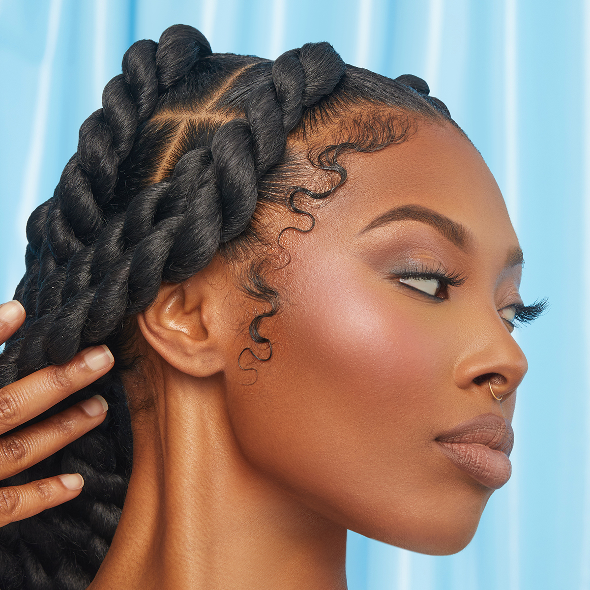 Close-up of a woman with smooth, styled edges and thick twisted braids, showcasing sleek hair texture against a soft blue background.