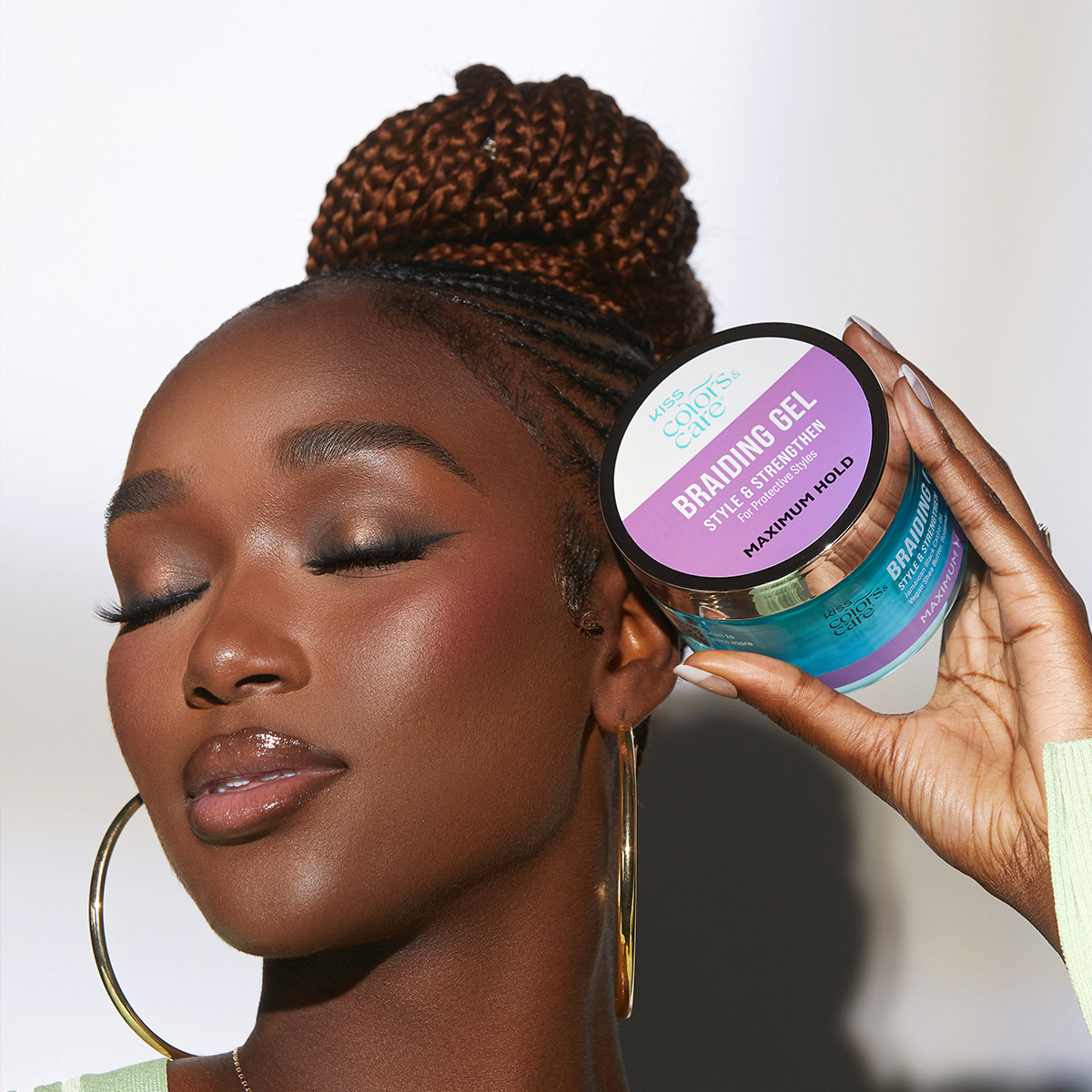 Woman with braided hair styled in a high bun holds a 6 oz container of KISS Colors &amp; Care Braiding Gel labeled \