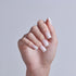 Close-up of a hand displaying white French manicure nails against a light gray background.