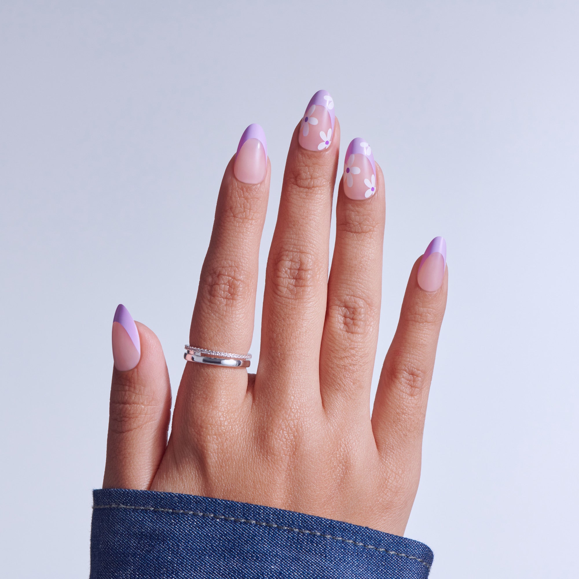 Manicured hand displaying purple ombre nails with floral design and silver ring.
