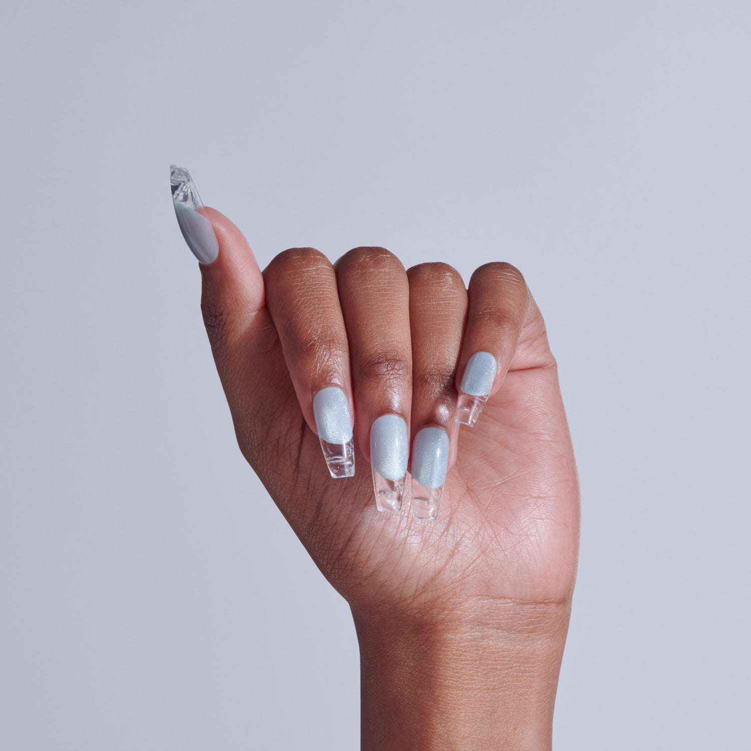 Hand displaying clear nail extensions with white sparkly nail polish against light gray background.