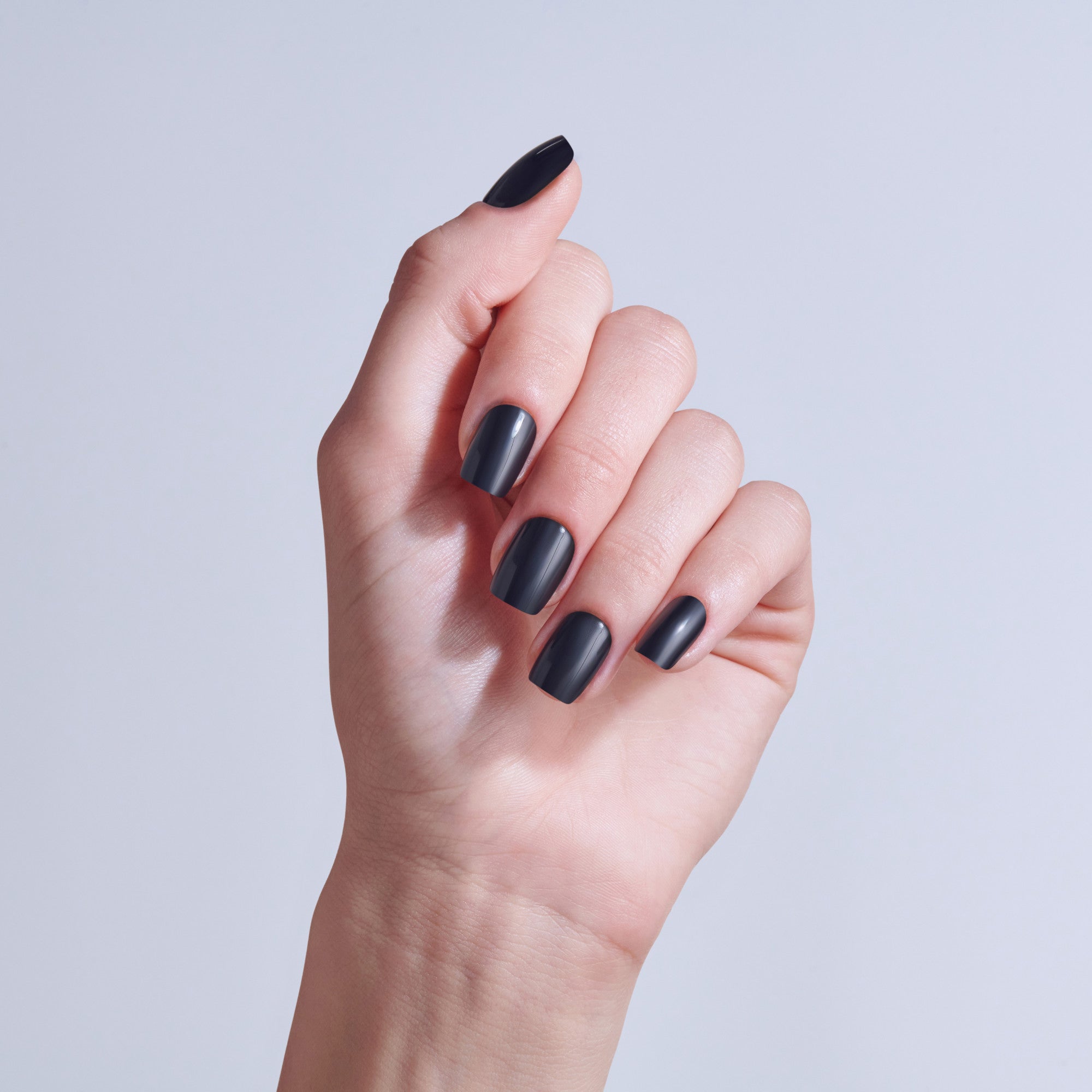 Hand displaying matte black nail polish on short, rounded nails against light background.