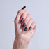 Hand displaying matte black nail polish on short, rounded nails against light background.