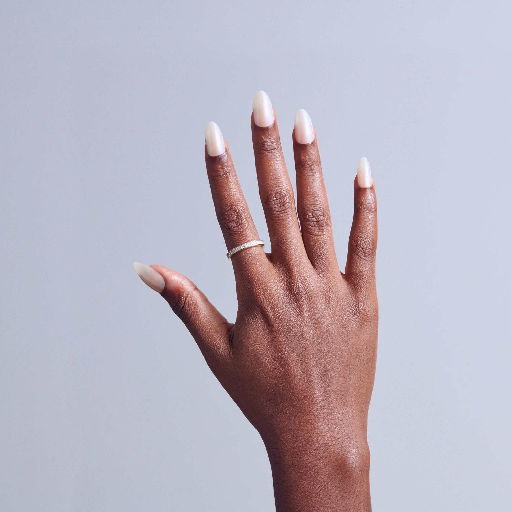 Hand with almond-shaped nails featuring white ombre tips and a silver ring against gray background.