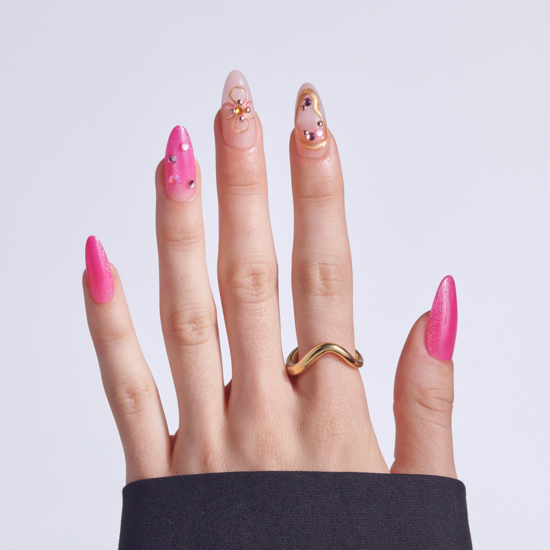 Hand with pink glitter almond nails decorated with rhinestones and gold charms.