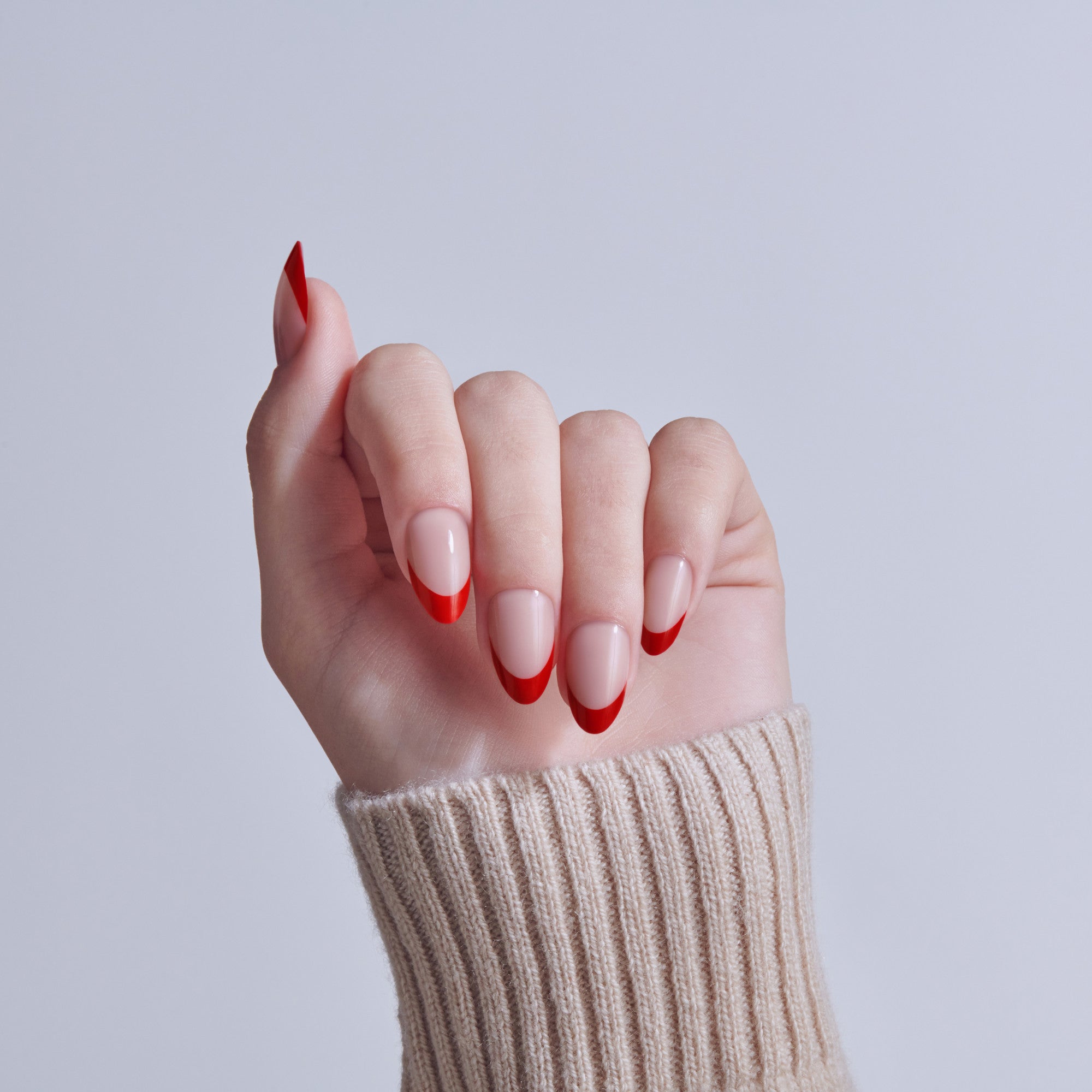 Hand with red and white ombre nail polish design, wearing beige sweater cuff.