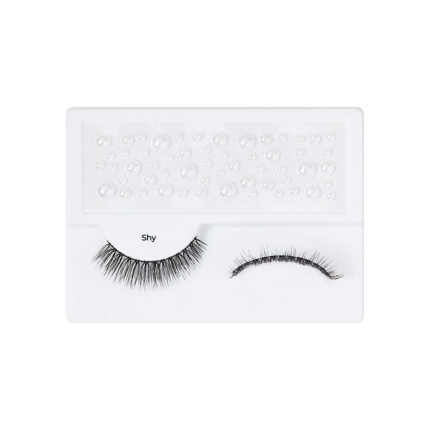 The image features a pair of false eyelashes displayed on a white tray. The lashes are labeled "Shy" and are arranged neatly, with one set appearing fuller and longer than the other. The tray has a textured surface with small, raised dots, likely designed to hold the lashes securely in place. The overall presentation is clean and minimalistic, emphasizing the eyelashes themselves.